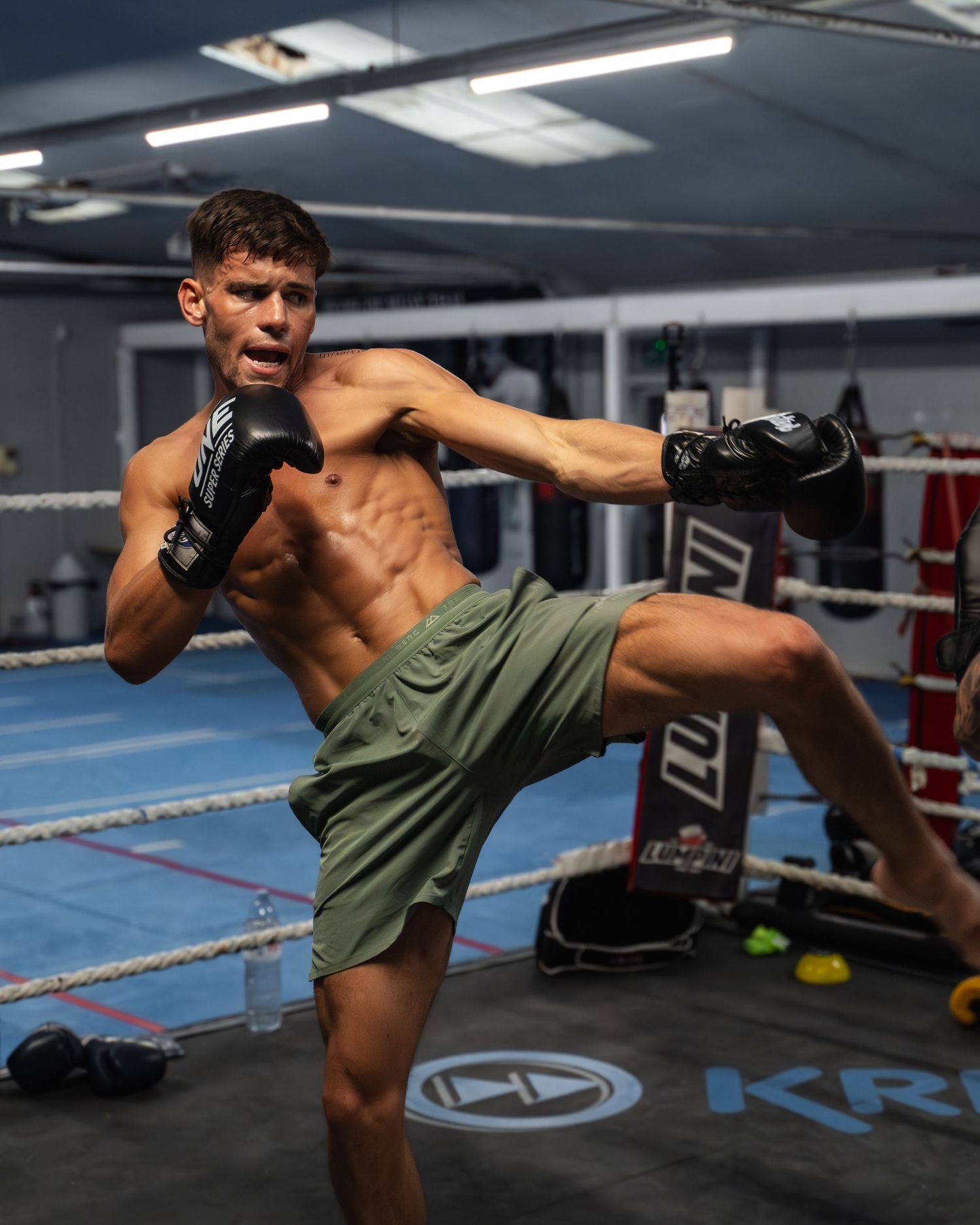 Martial artist practicing high kicks in a modern training facility with boxing rings.