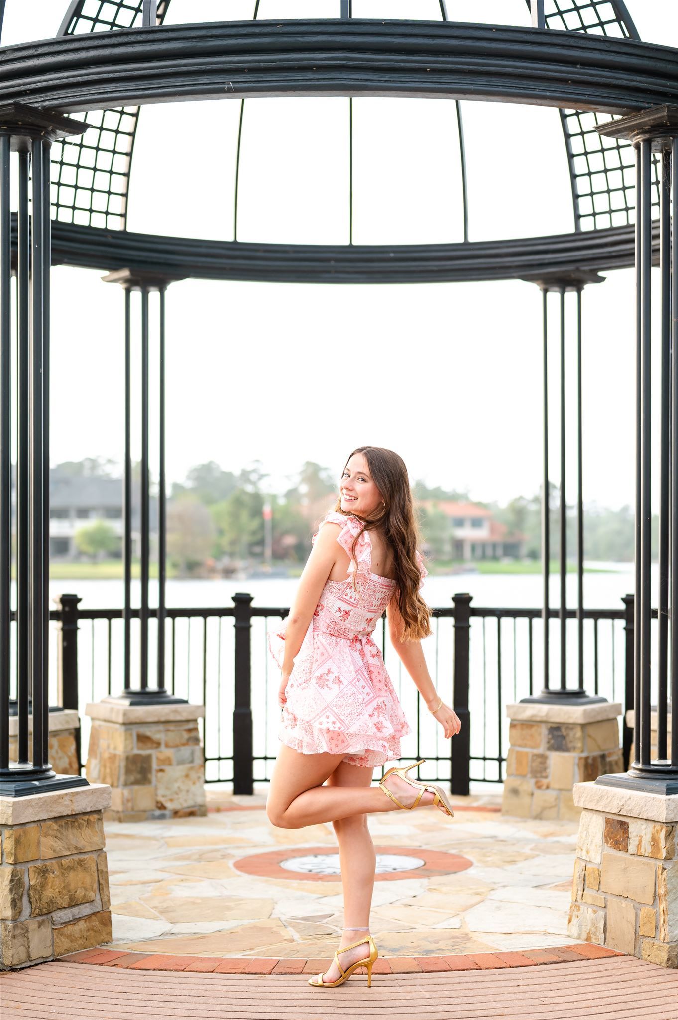 A natural light photoshoot shows dancer in peach dress posing gracefully in stone gazebo by waterfront.