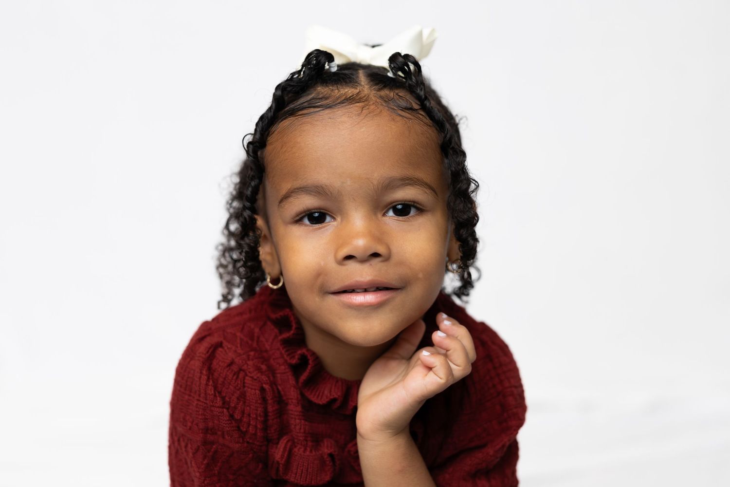 Studio portrait of a child in a burgundy sweater with curly hair and hair clips.