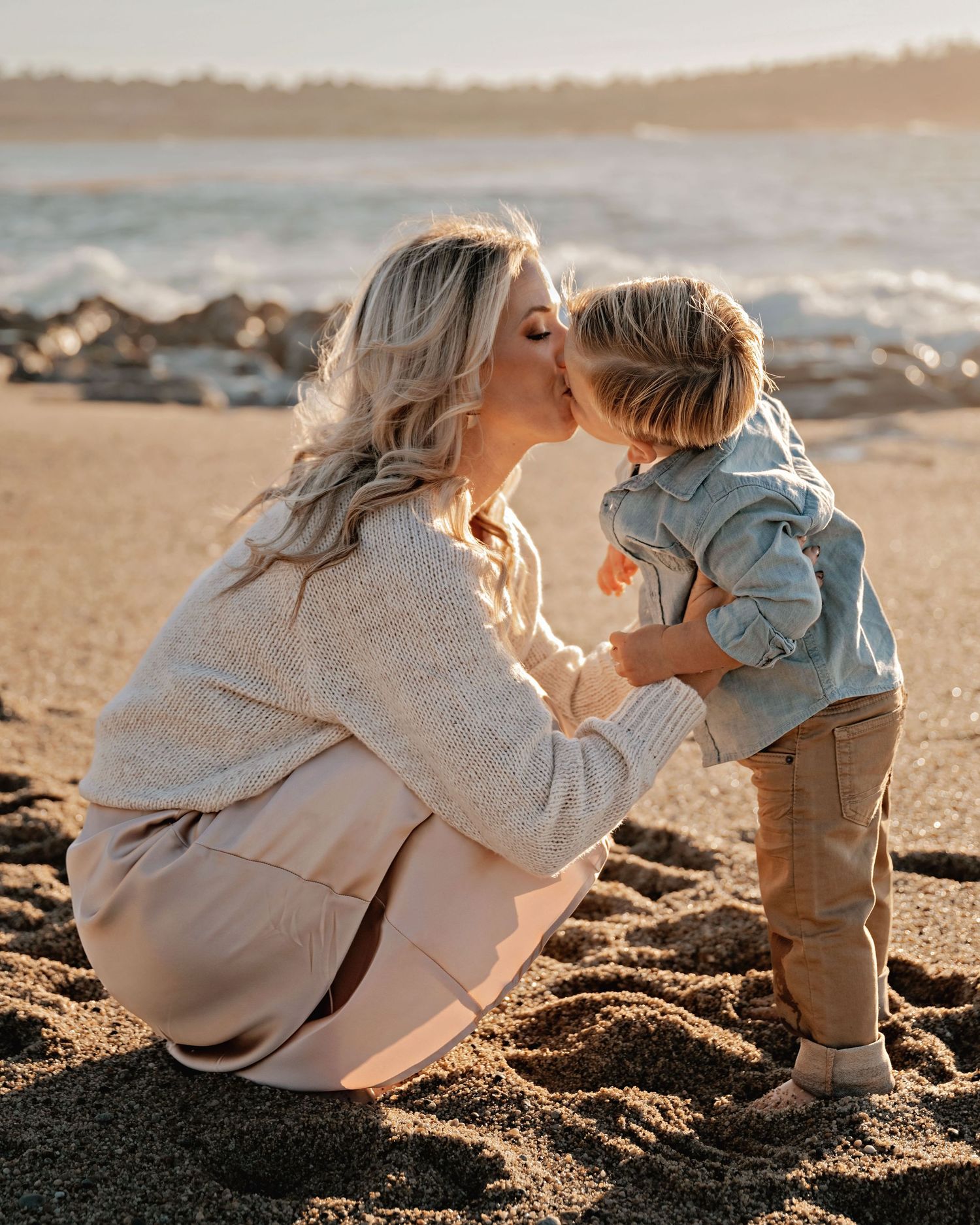 Mother and child playing together on sandy beach at sunset.