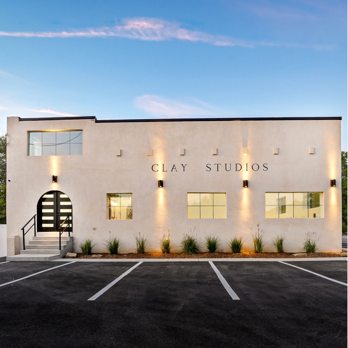 Modern white commercial building exterior with large windows and illuminated entrance in Clay Studios during twilight.