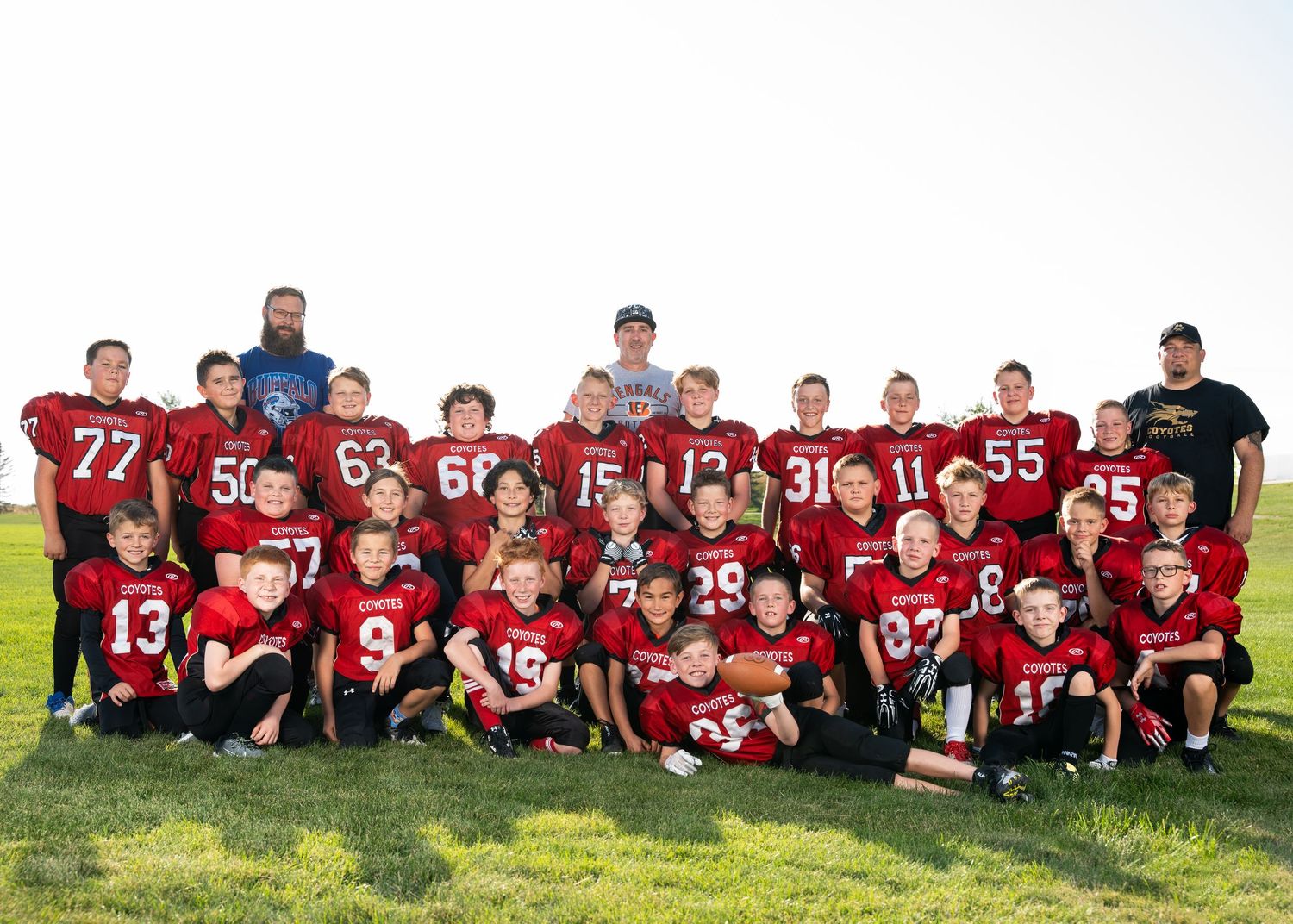 Youth football team in red jerseys posing together on grass field for team photo.