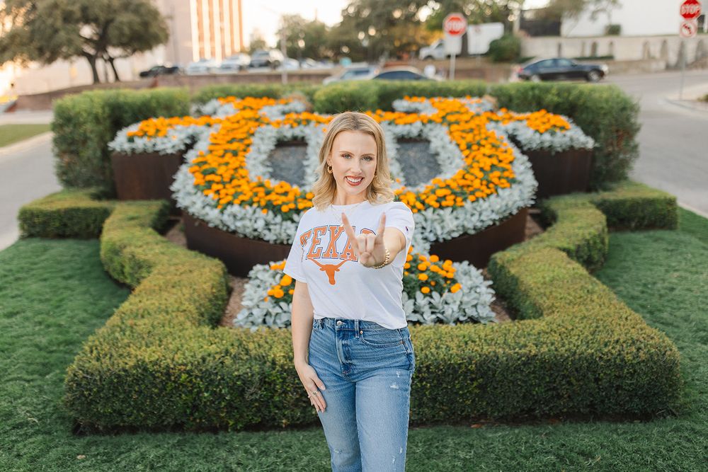 Someone wearing denim overalls stands in a manicured garden with vibrant orange marigolds and trimmed hedges.