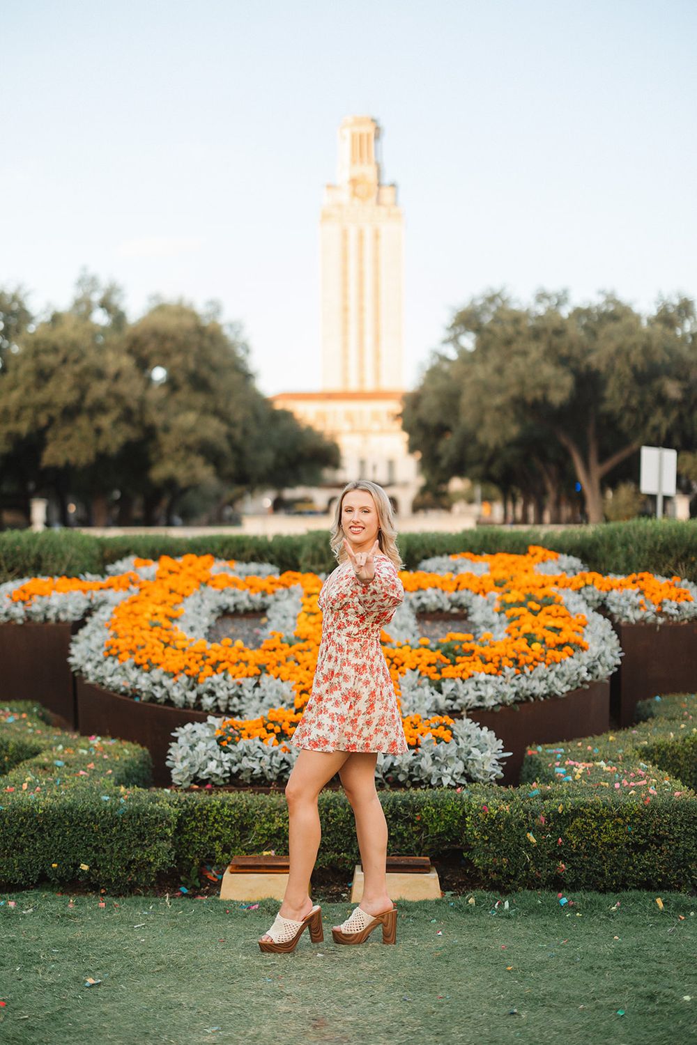 A floral scene with orange flowers forming the University of Texas logo in front of the UT Tower at sunset.