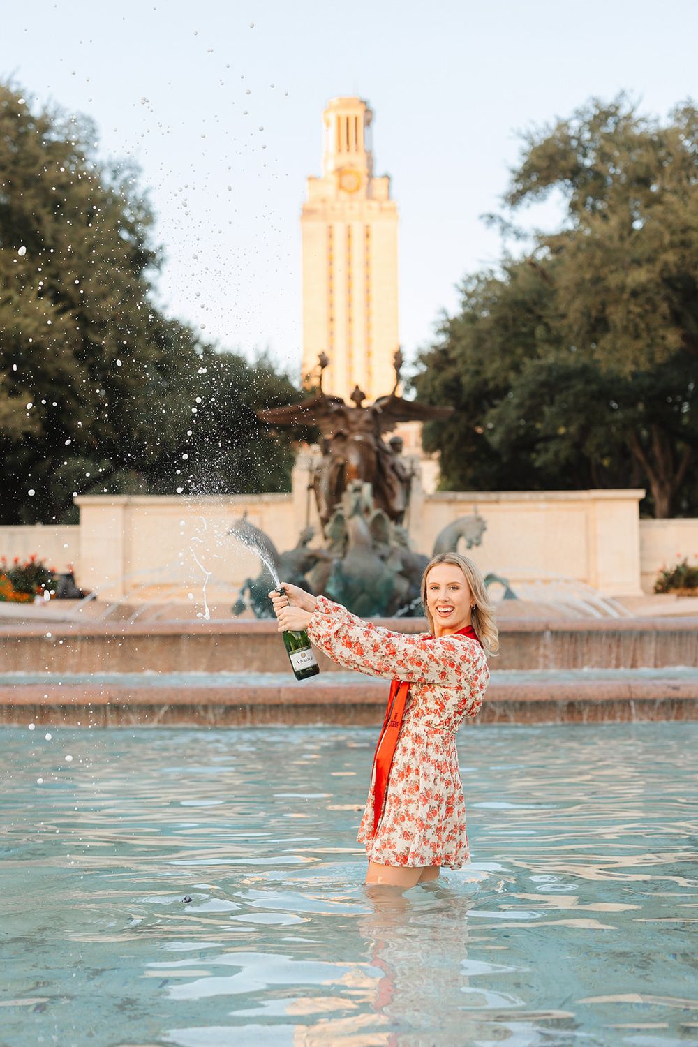 Person splashes in fountain water near UT Austin Tower and Littlefield Fountain on campus during golden hour.