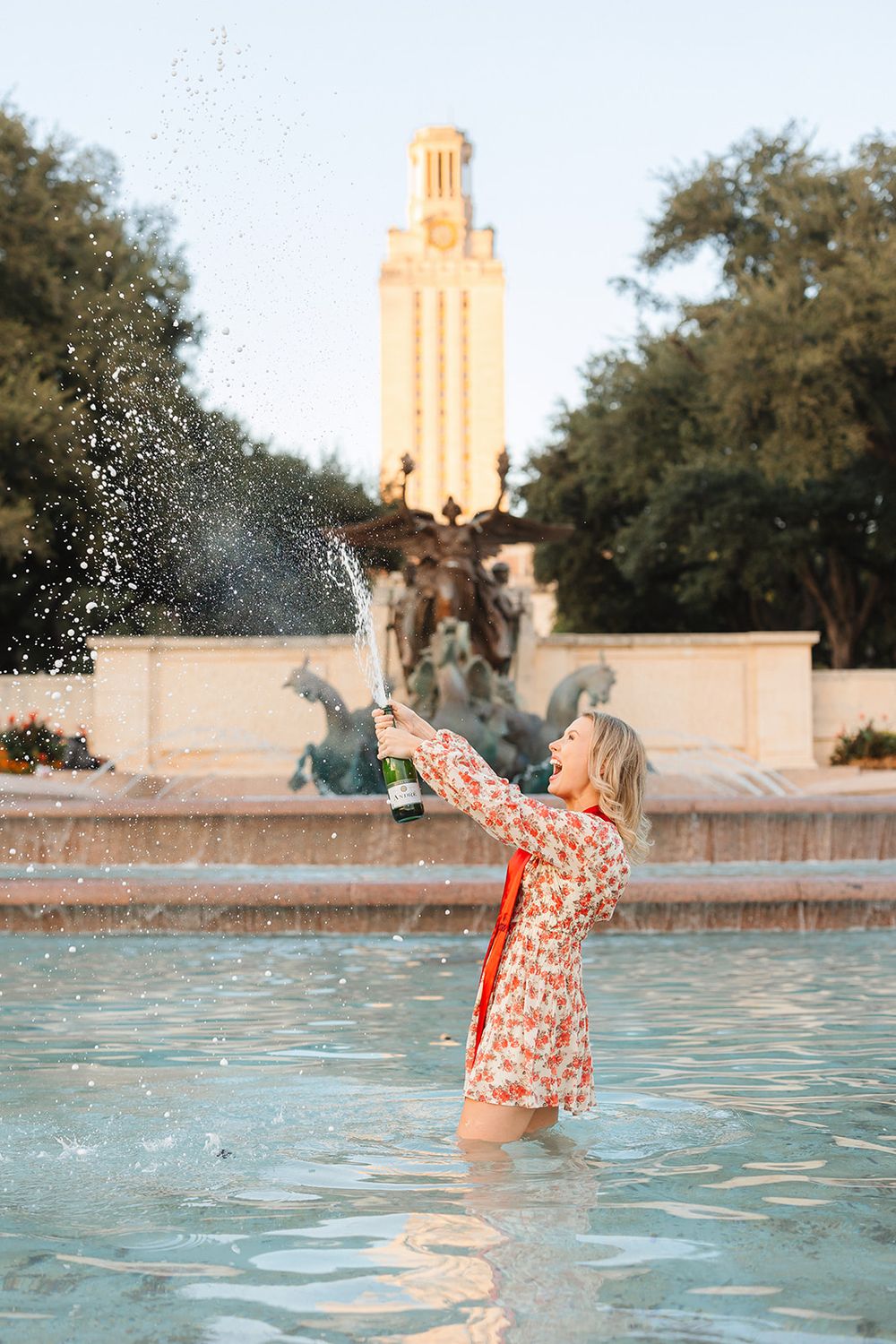 Someone plays in the fountain at University of Texas with the iconic tower visible in the background at sunset.
