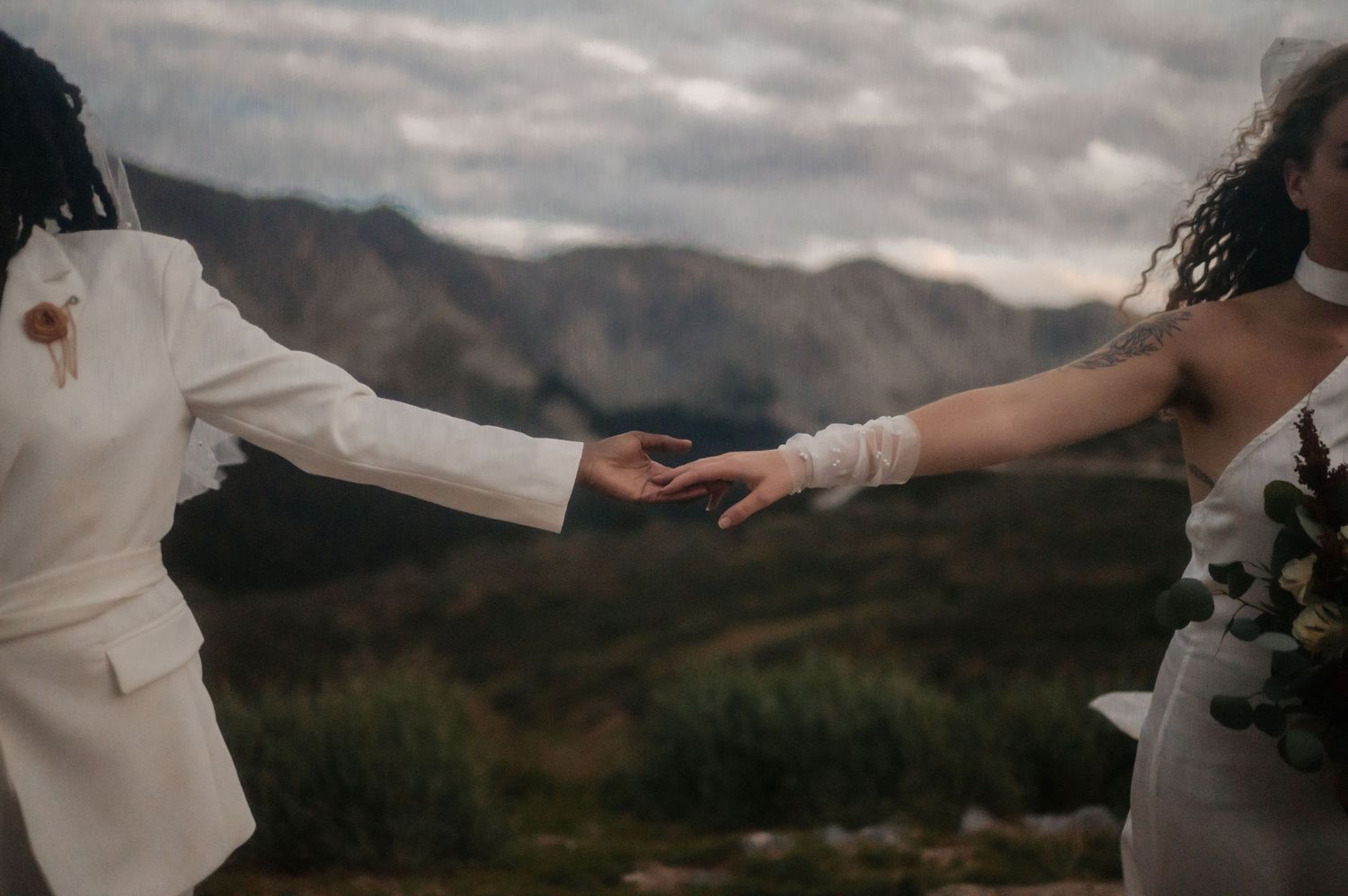 Silhouetted figures in white against a dramatic mountain backdrop reach for each other at sunset.