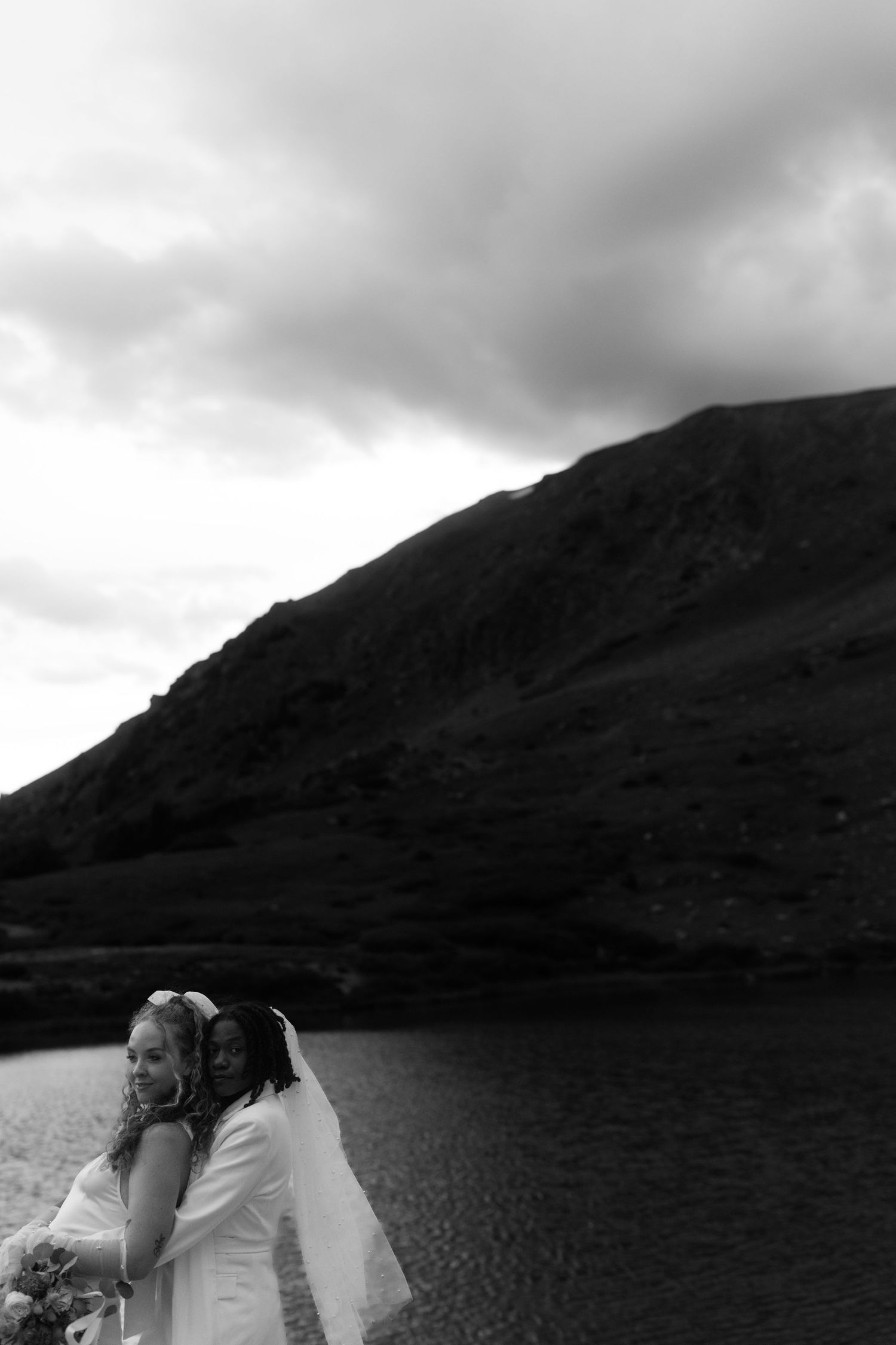 Black and white photograph of a couple embracing by a mountain lake.