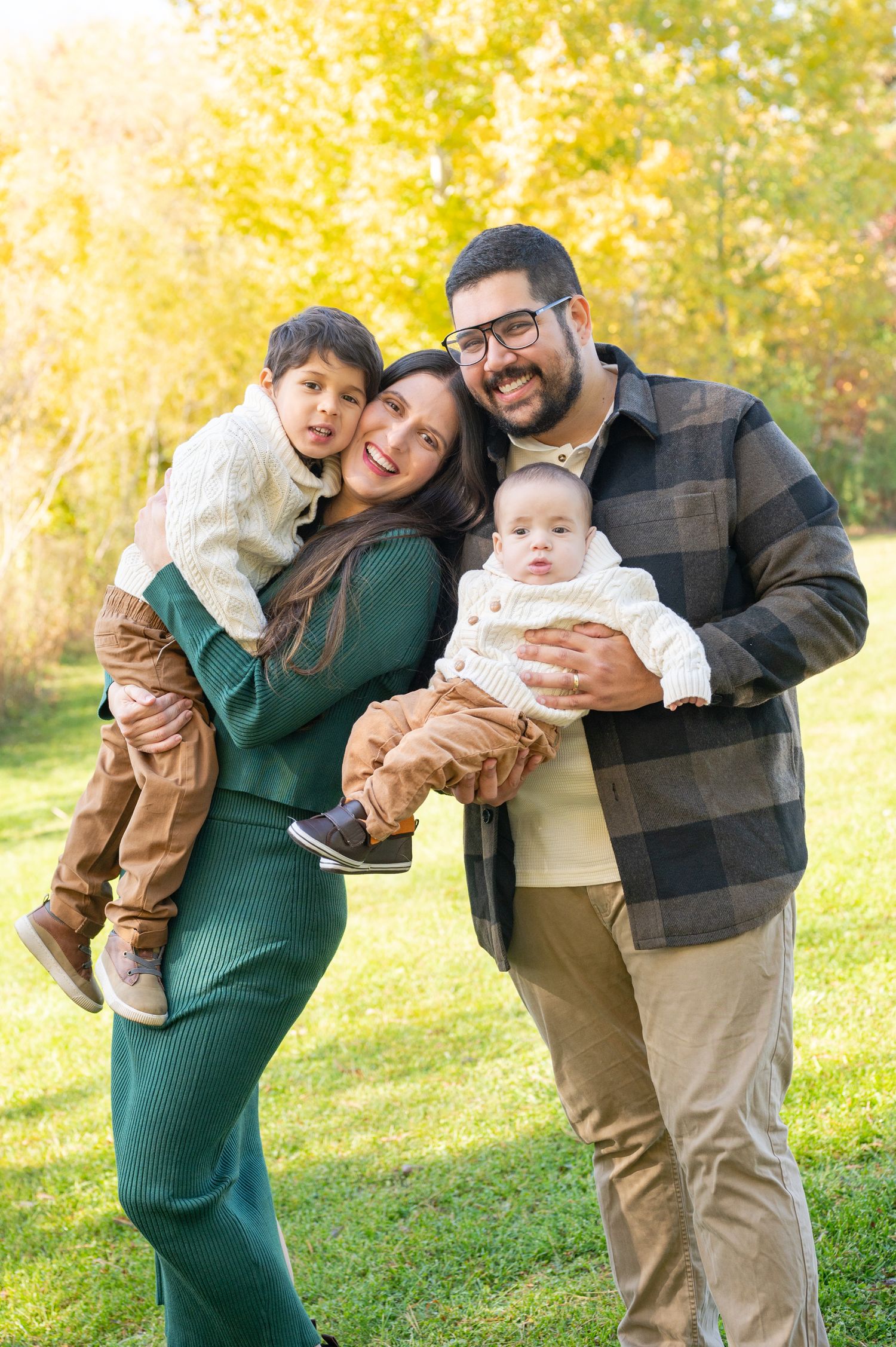 Family shares joyful moments together during fall photoshoot with yellow leaves in background.