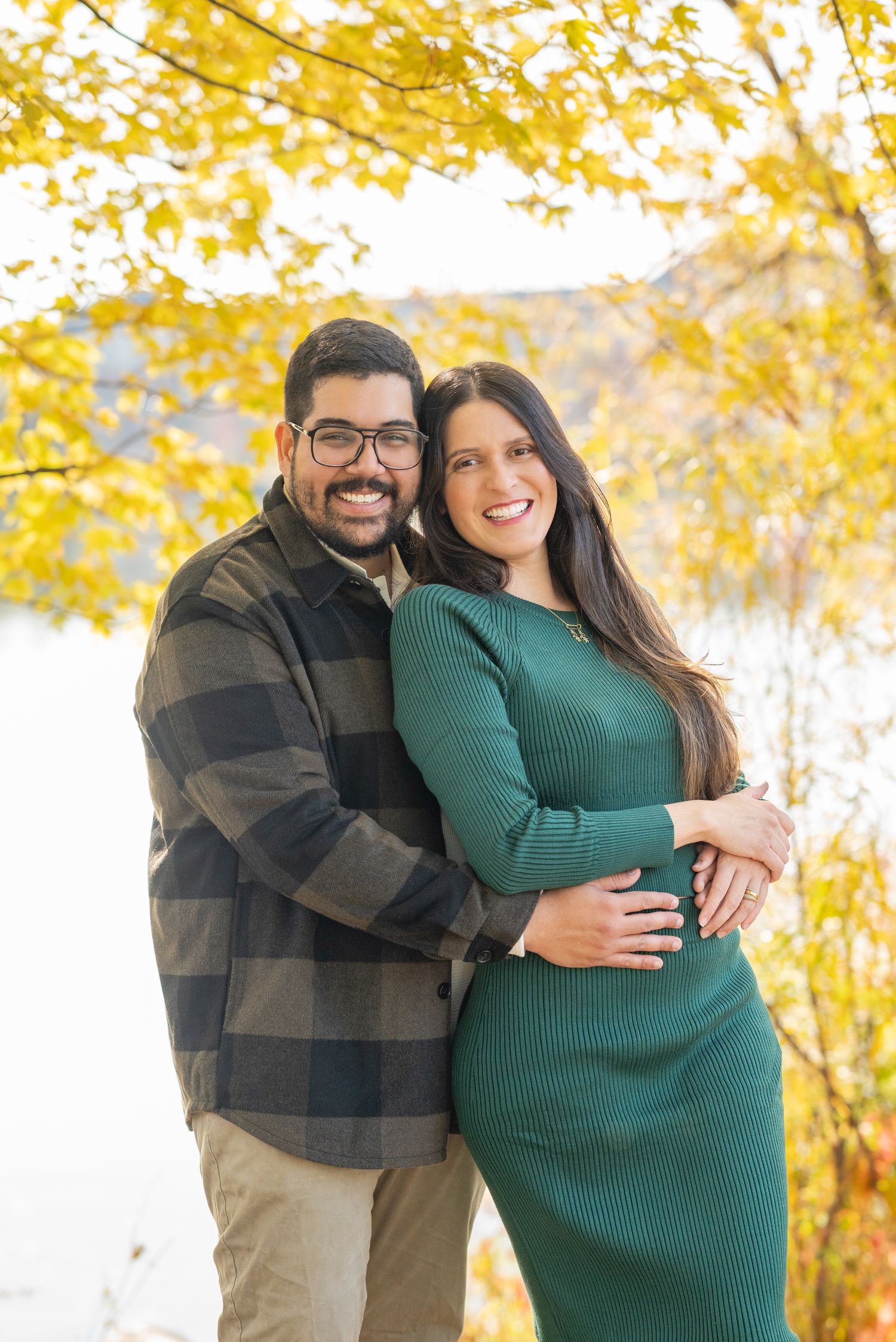 Couple embraces during autumn maternity photoshoot with golden foliage.
