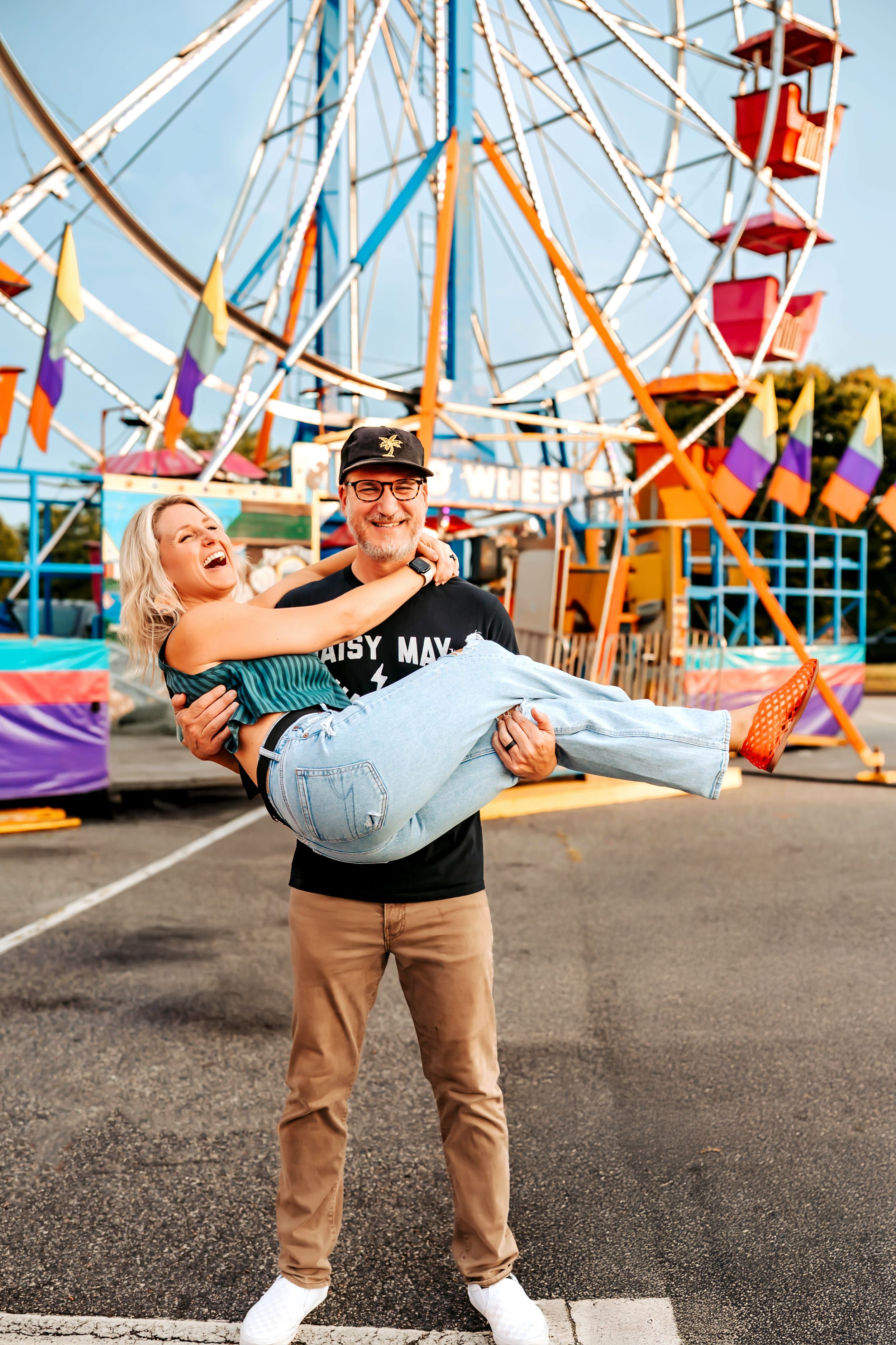 Two people sharing a playful moment at an amusement park with a colorful Ferris wheel in the background.