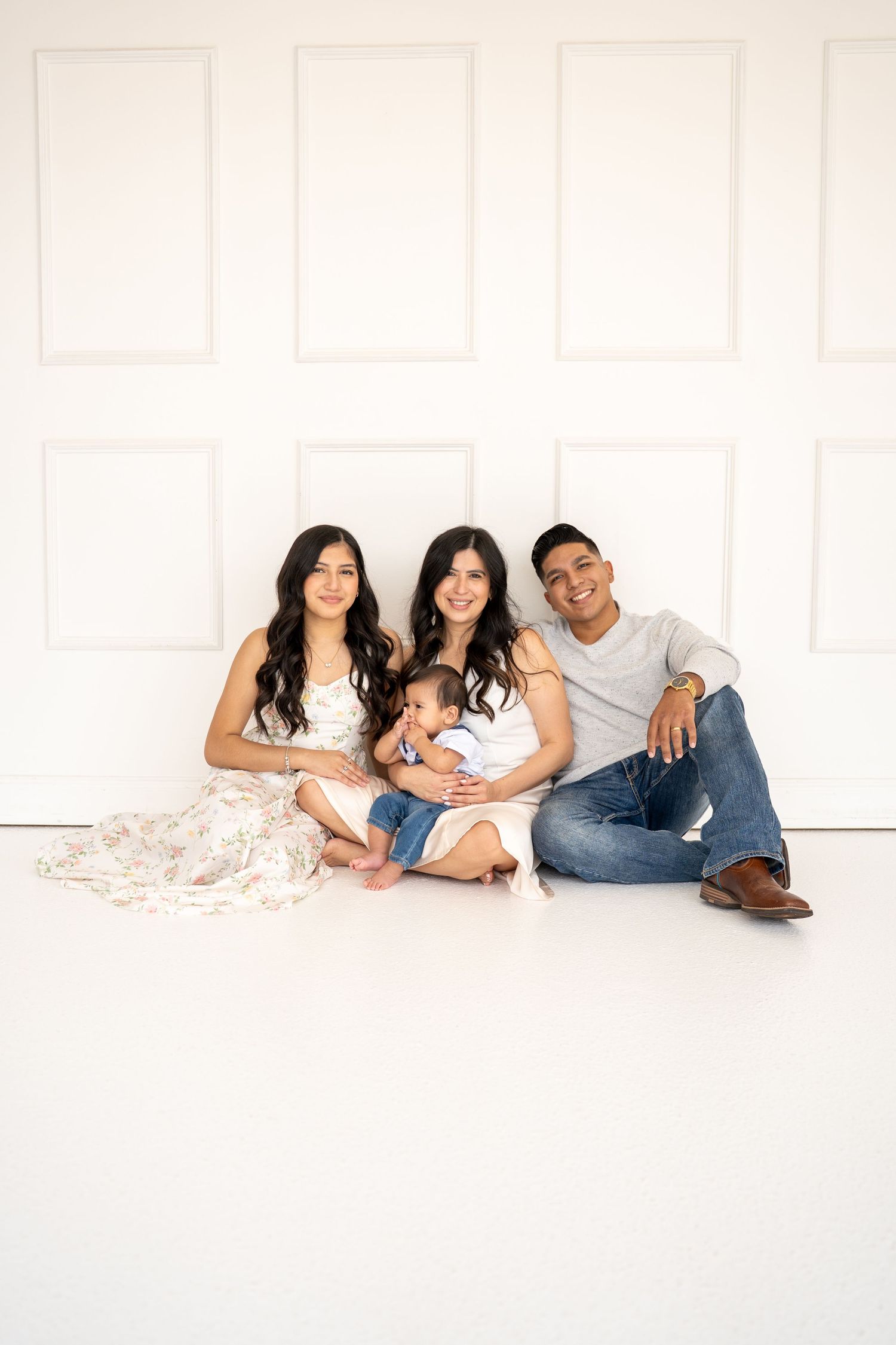 Family relaxing together on white floor wearing coordinated casual outfits.