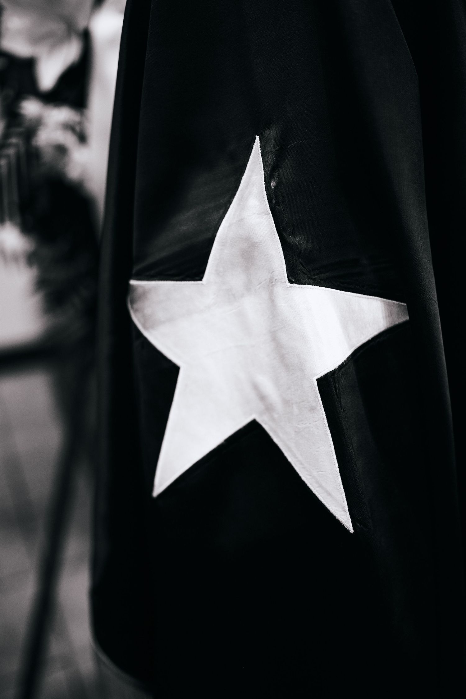 A white star symbol on black fabric photographed in black and white against a blurred background.