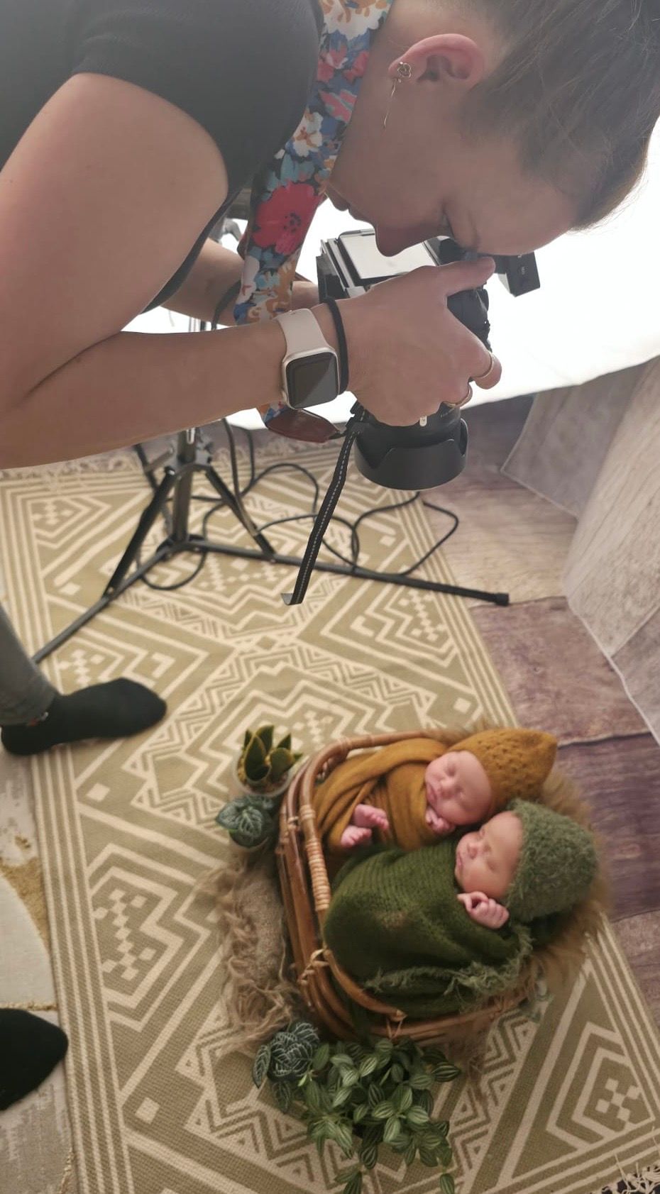 Overhead view of photographer capturing newborn portrait in basket with green blanket and floral decor.