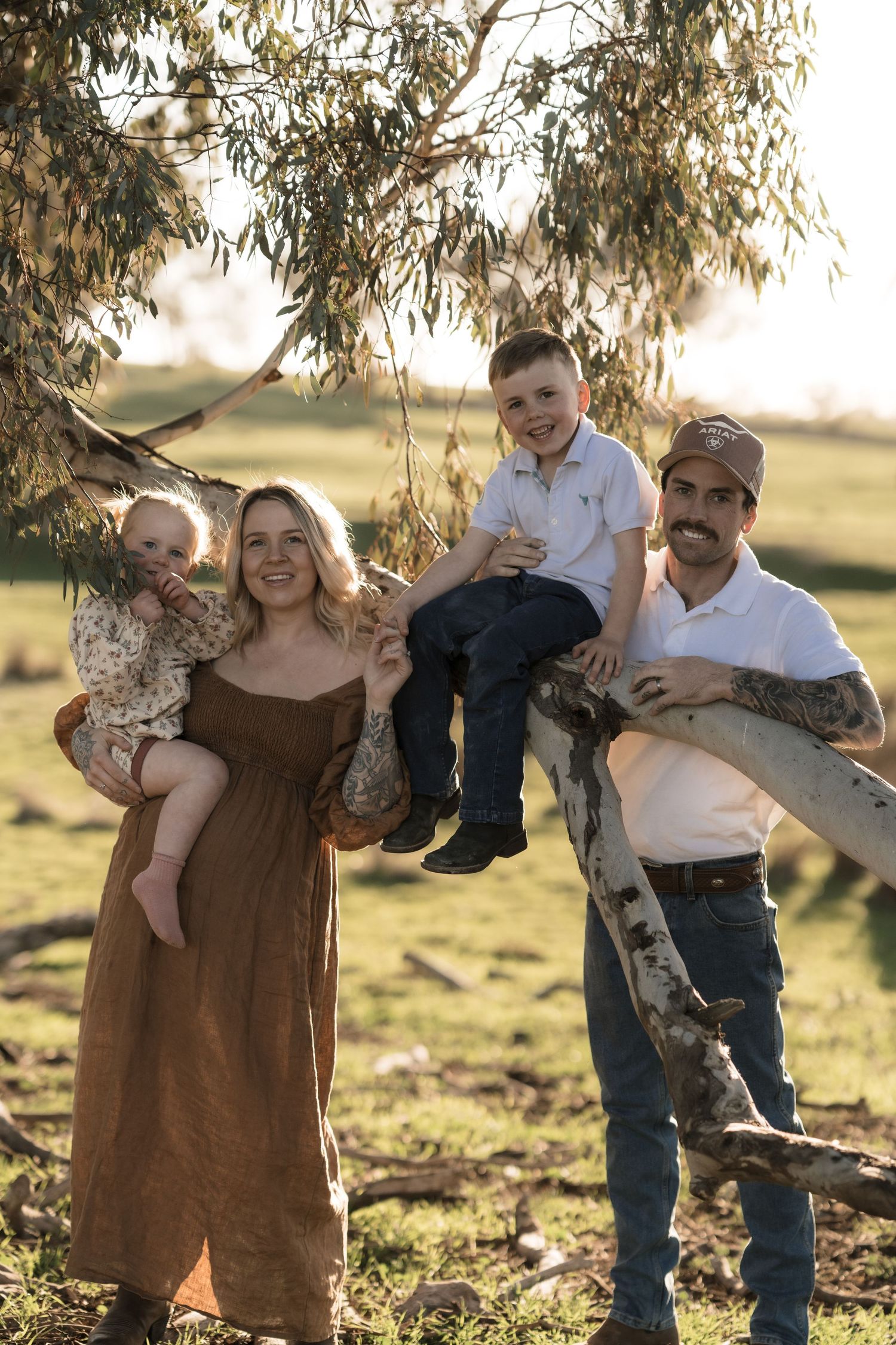 A family poses together under a eucalyptus tree during a golden hour photoshoot.