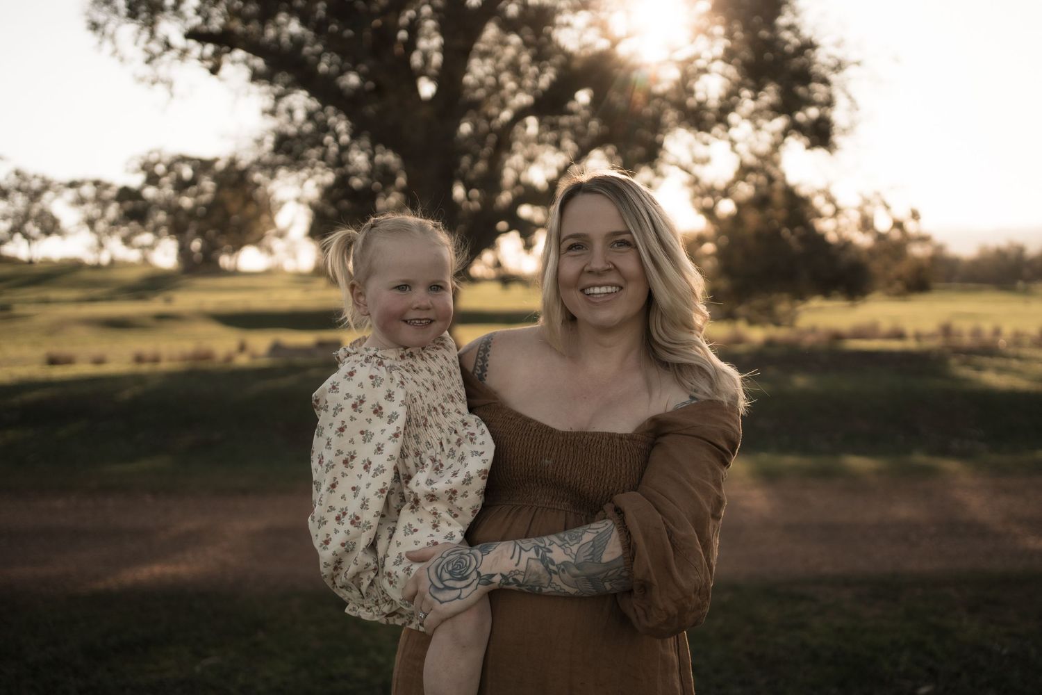 Candid family photo session at sunset with warm golden light filtering through trees in a rustic outdoor setting.