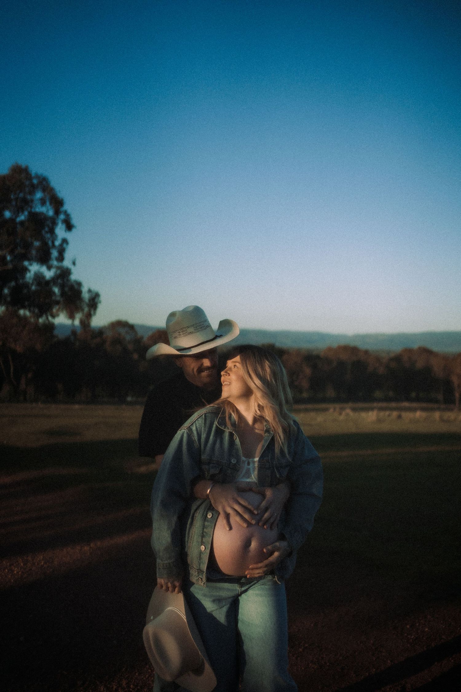 A couple shares an intimate moment during sunset in a rural setting.