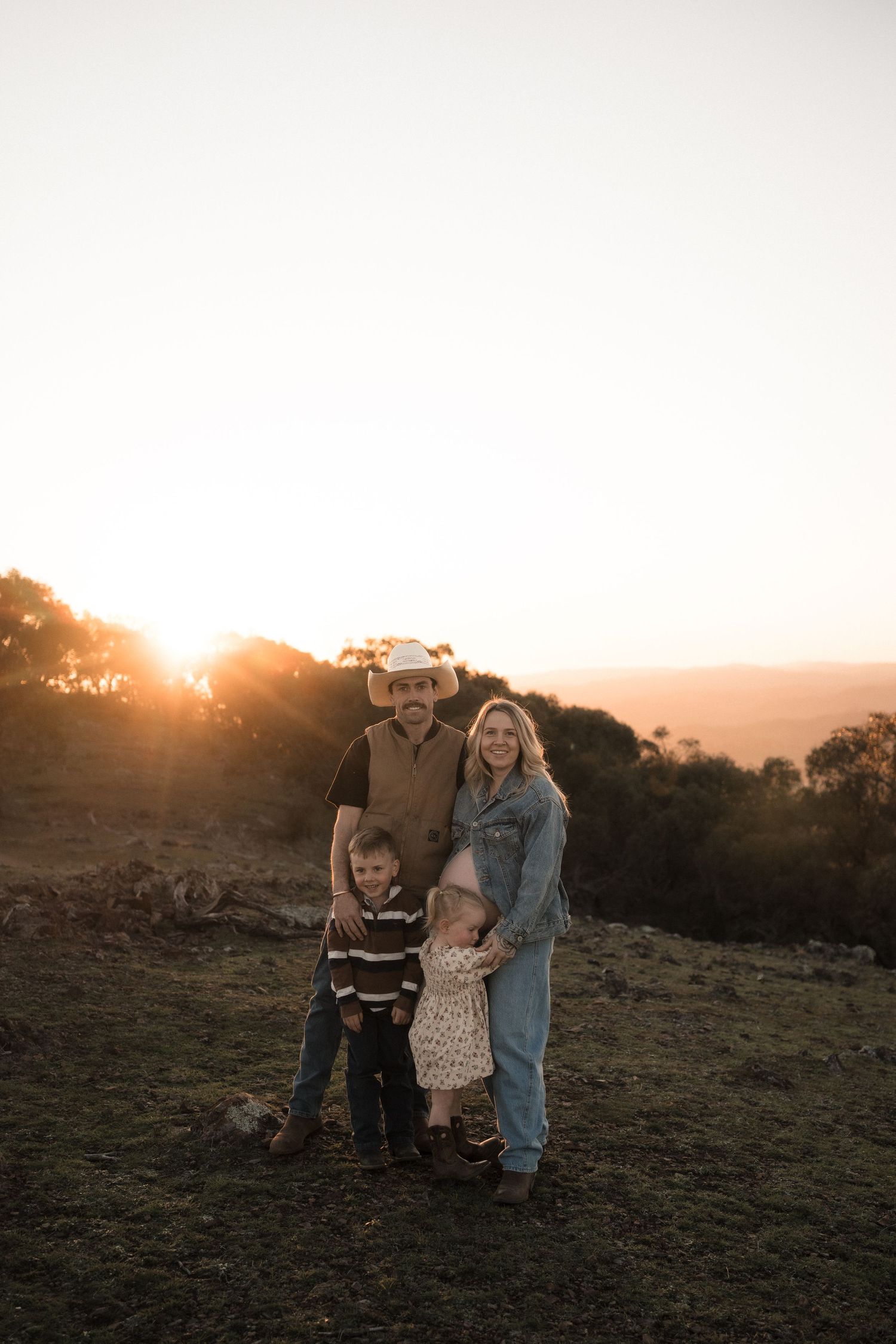 Family walking together on a hilltop during sunset with dramatic lighting and natural landscape.