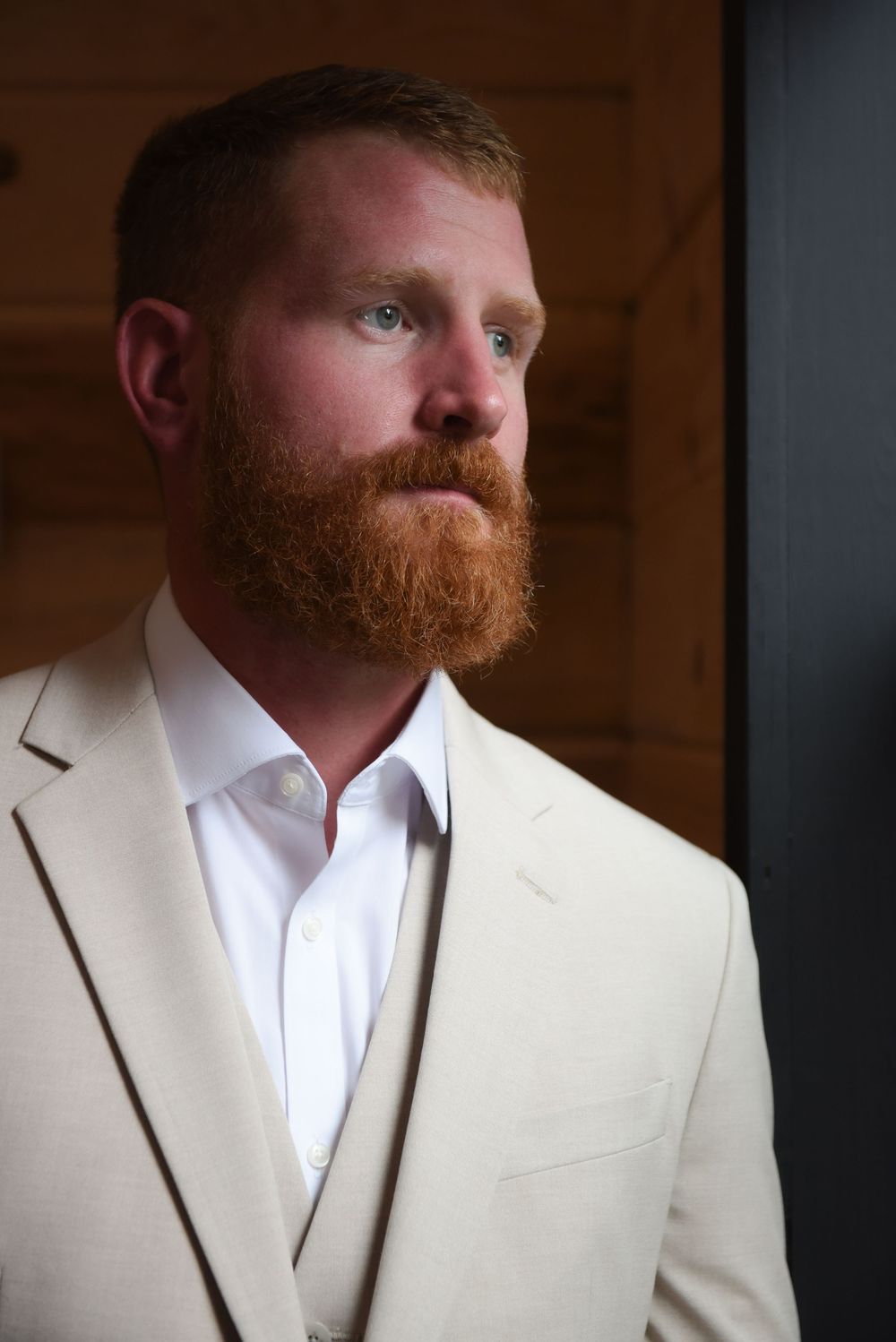 Portrait of groom wearing cream suit jacket with white shirt in dramatic lighting.