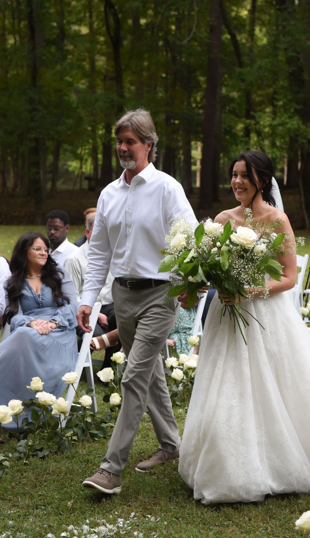 A wedding celebration takes place in a lush green garden setting with white floral decorations.