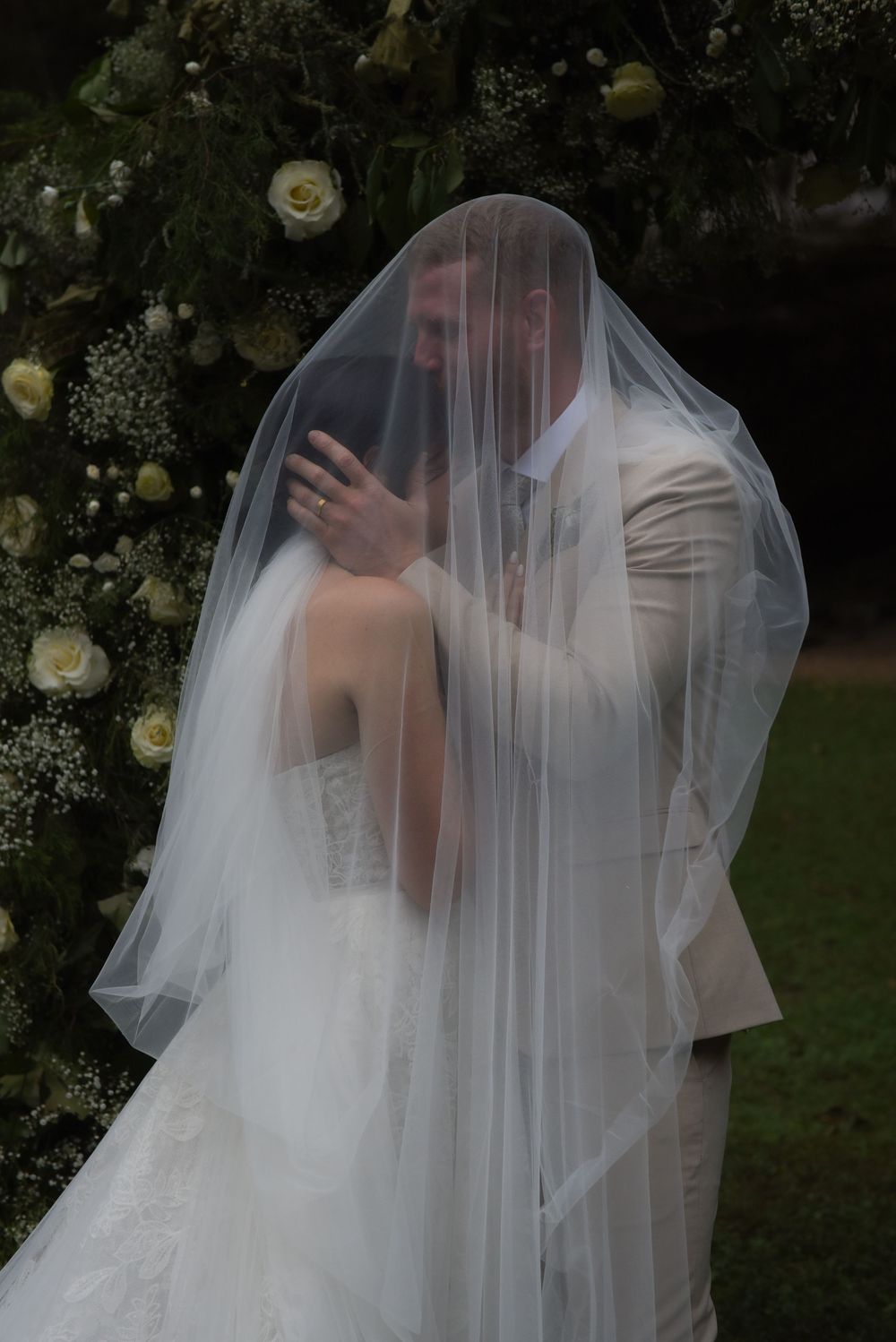 A flowing white wedding veil creates a romantic silhouette against a garden backdrop.