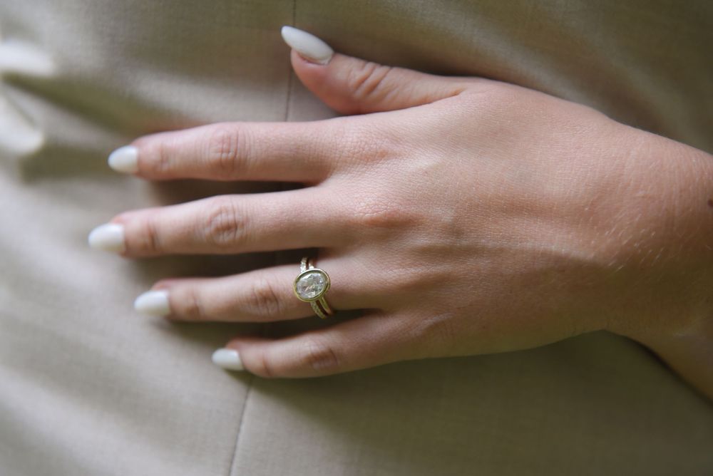 A delicate engagement ring sparkles on a hand against a soft neutral background.