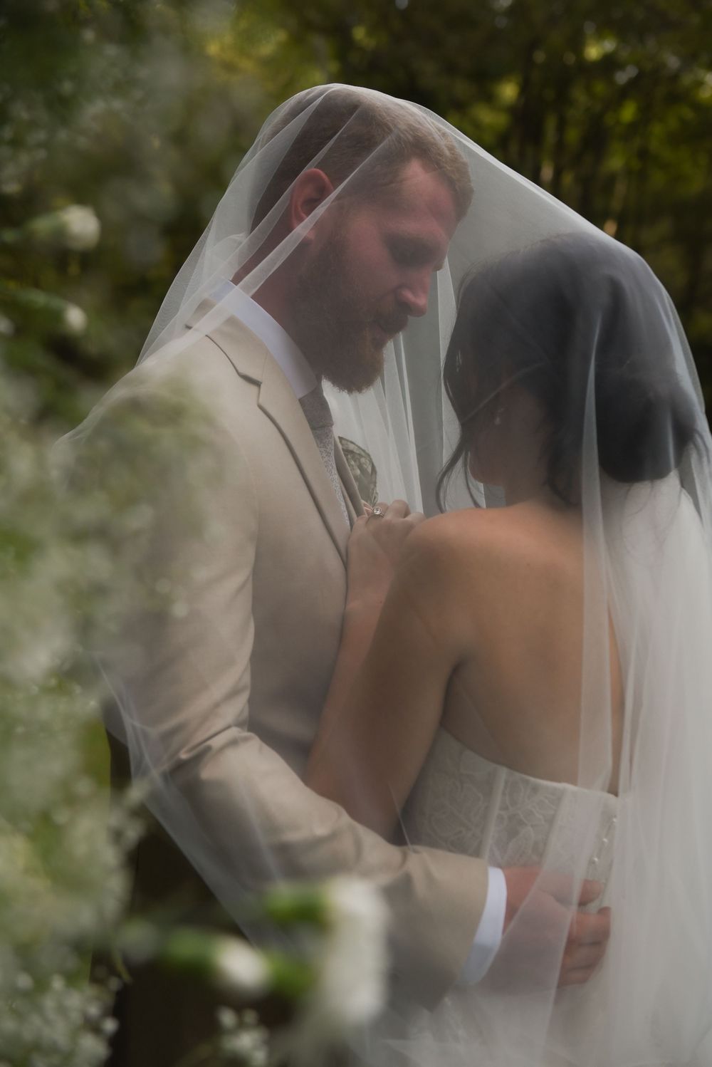 A romantic wedding moment captured through a sheer veil in a garden setting.