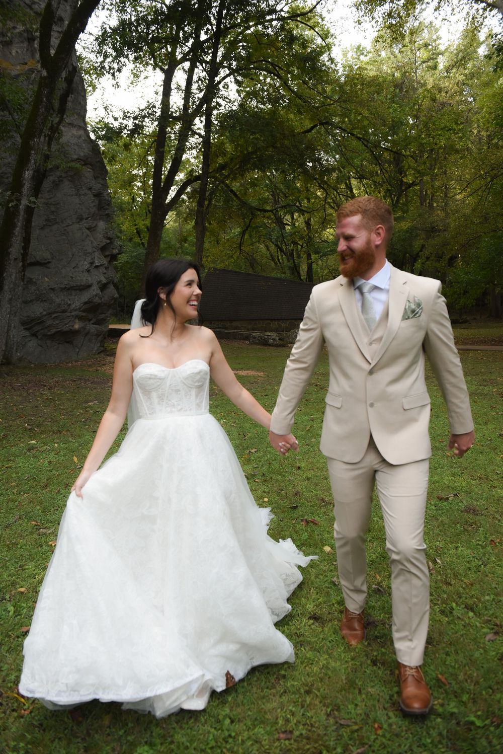 A couple walks hand in hand through a garden setting in wedding attire.