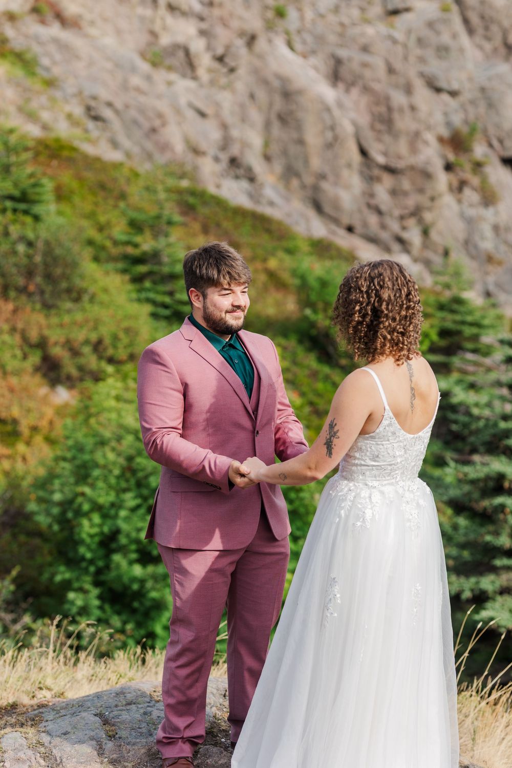 A wedding couple stands together on a scenic mountainside path with greenery in the background.