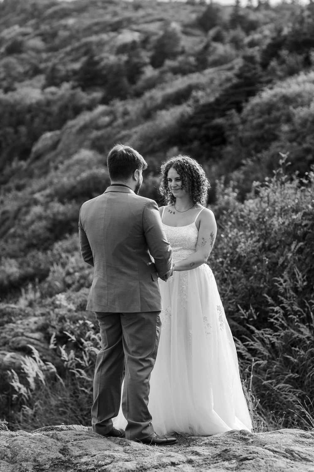 Bride and groom sitting together on mountainside ledge during black and white outdoor wedding photoshoot.