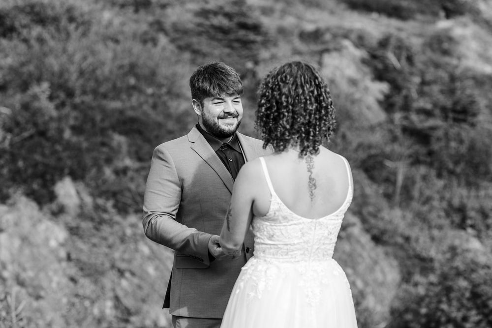 A romantic black and white portrait of a couple sharing a joyful moment together in their wedding attire outdoors.