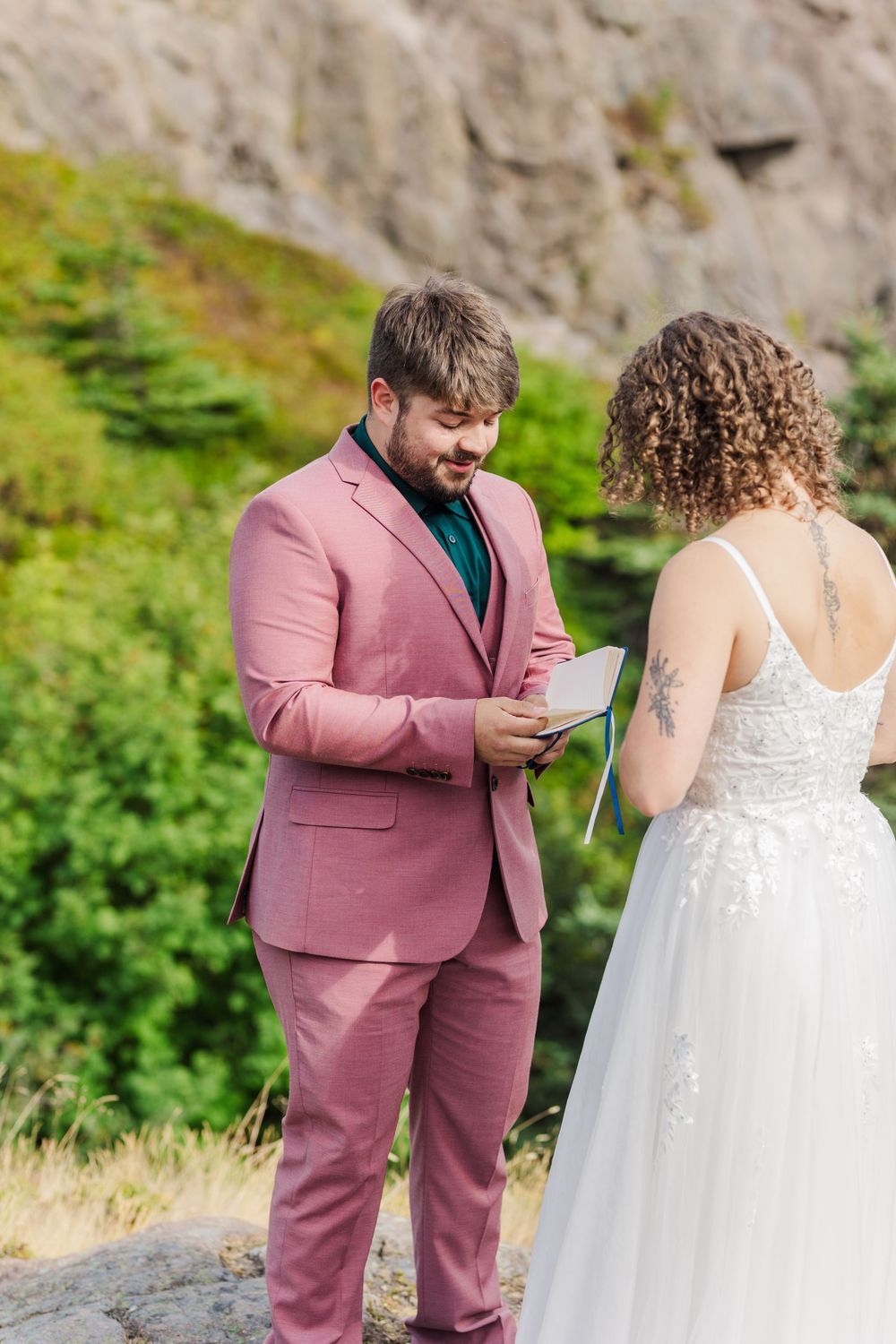 A couple shares an intimate first look moment with the groom wearing a rose-colored suit and bride in white dress.