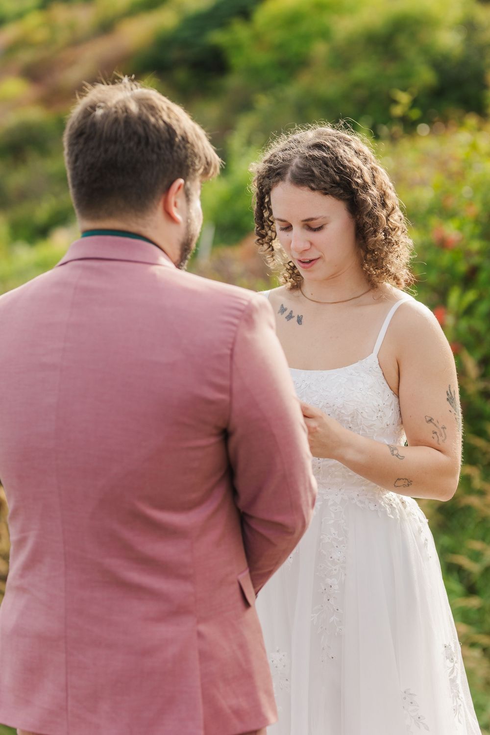 A couple in pink and white attire hold hands in a sunlit garden during an intimate outdoor wedding moment.