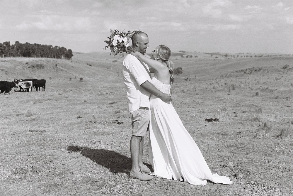 Young child in white clothing walking across rural grassland while under adult supervision in vintage black and white photo.