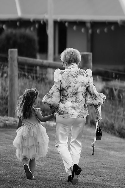 Two young children in formal wear run through a grassy field in black and white photos.
