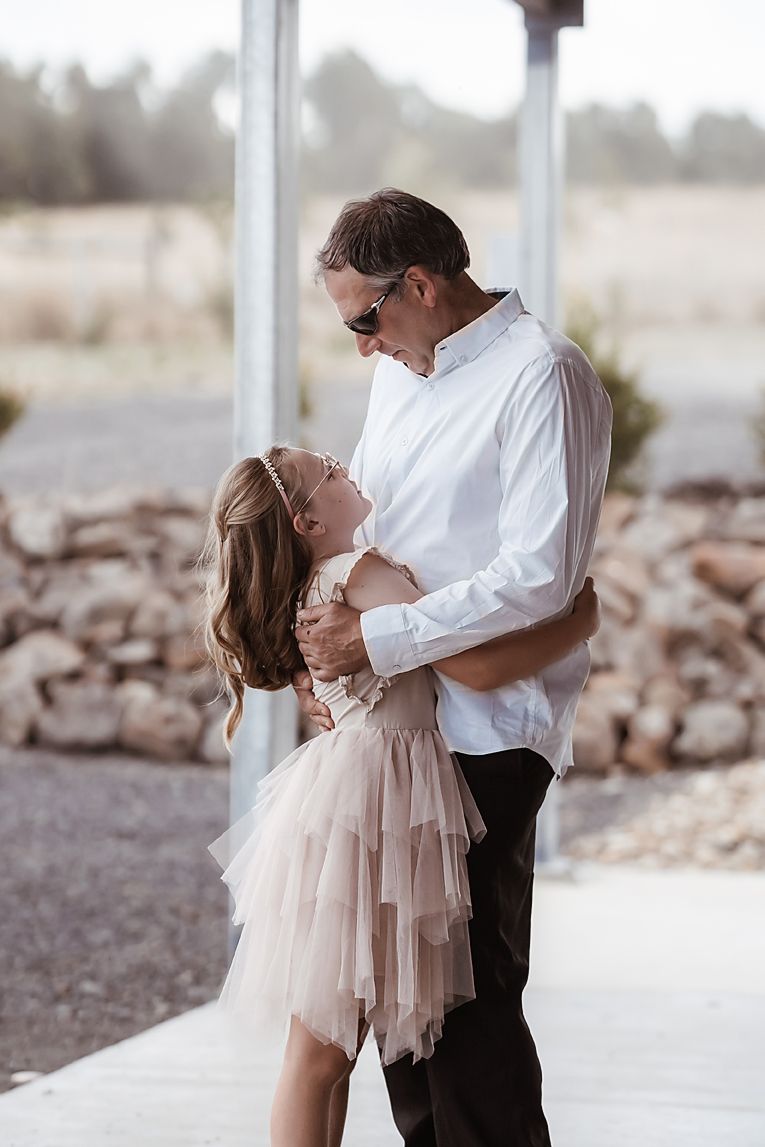 A romantic moment between two people dancing, with the woman wearing a flowy tulle dress in a rustic outdoor setting.