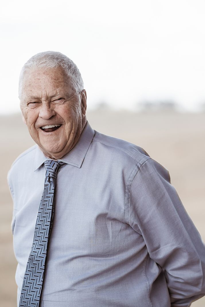 Senior man in dress shirt and tie laughs joyfully in natural lighting during outdoor photoshoot.