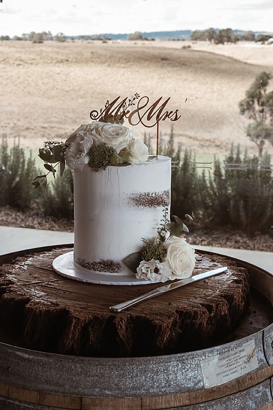 Elegant white wedding cake with floral decorations displayed on rustic wooden surface.