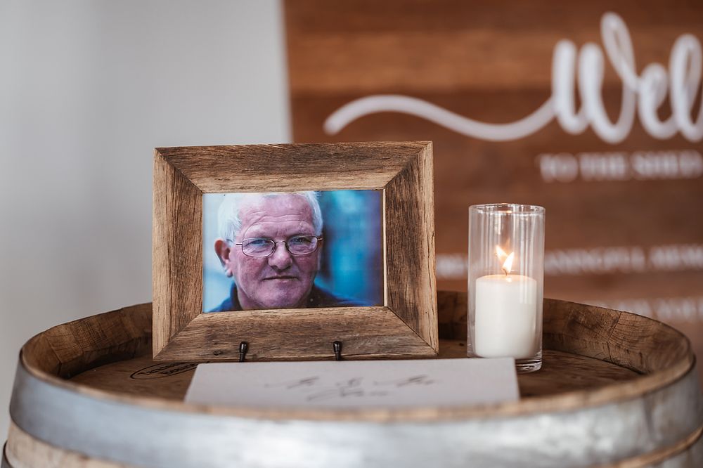 A framed photograph and lit candle rest on top of a rustic wooden wine barrel.