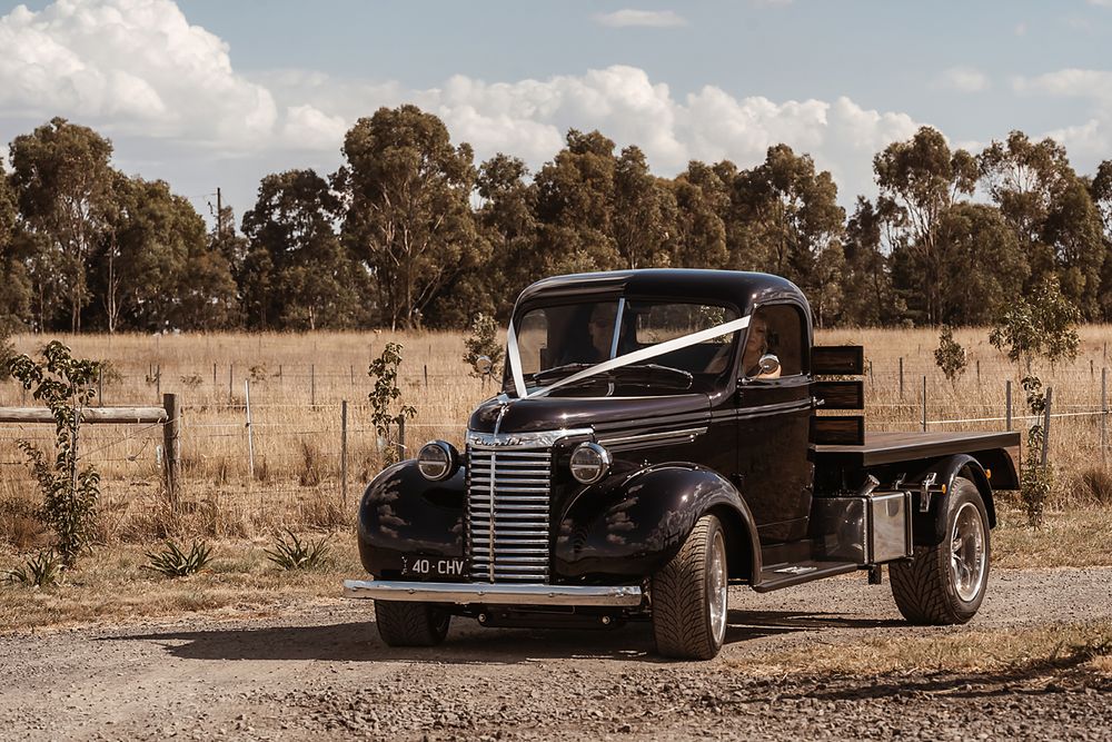 A vintage 1940s black pickup truck parked on a dirt road with trees in the background.