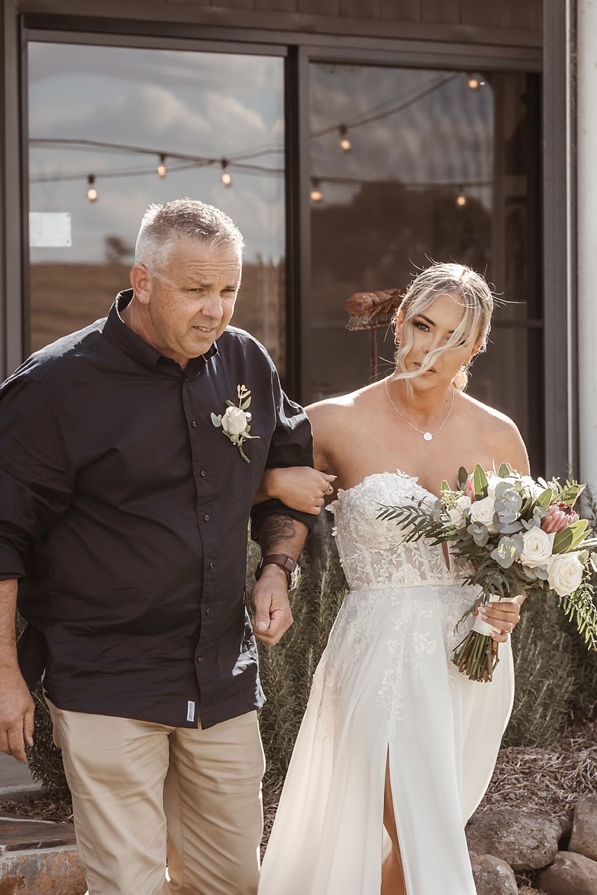 A couple walking together outdoors with the bride wearing a white strapless dress and carrying a floral bouquet.