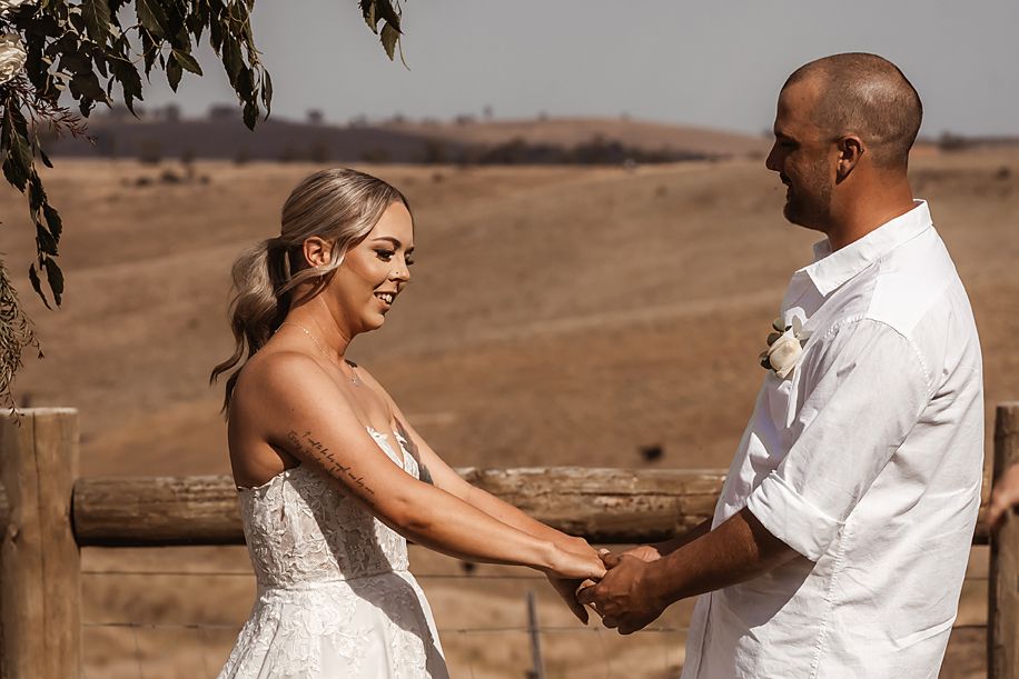 A tender moment between a couple in wedding attire against a rural landscape with rolling hills.