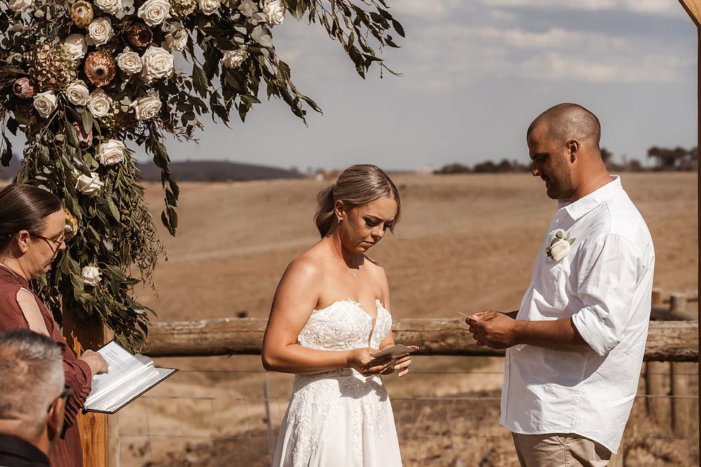 An intimate outdoor wedding ceremony with decorative floral arrangements in a rural setting.
