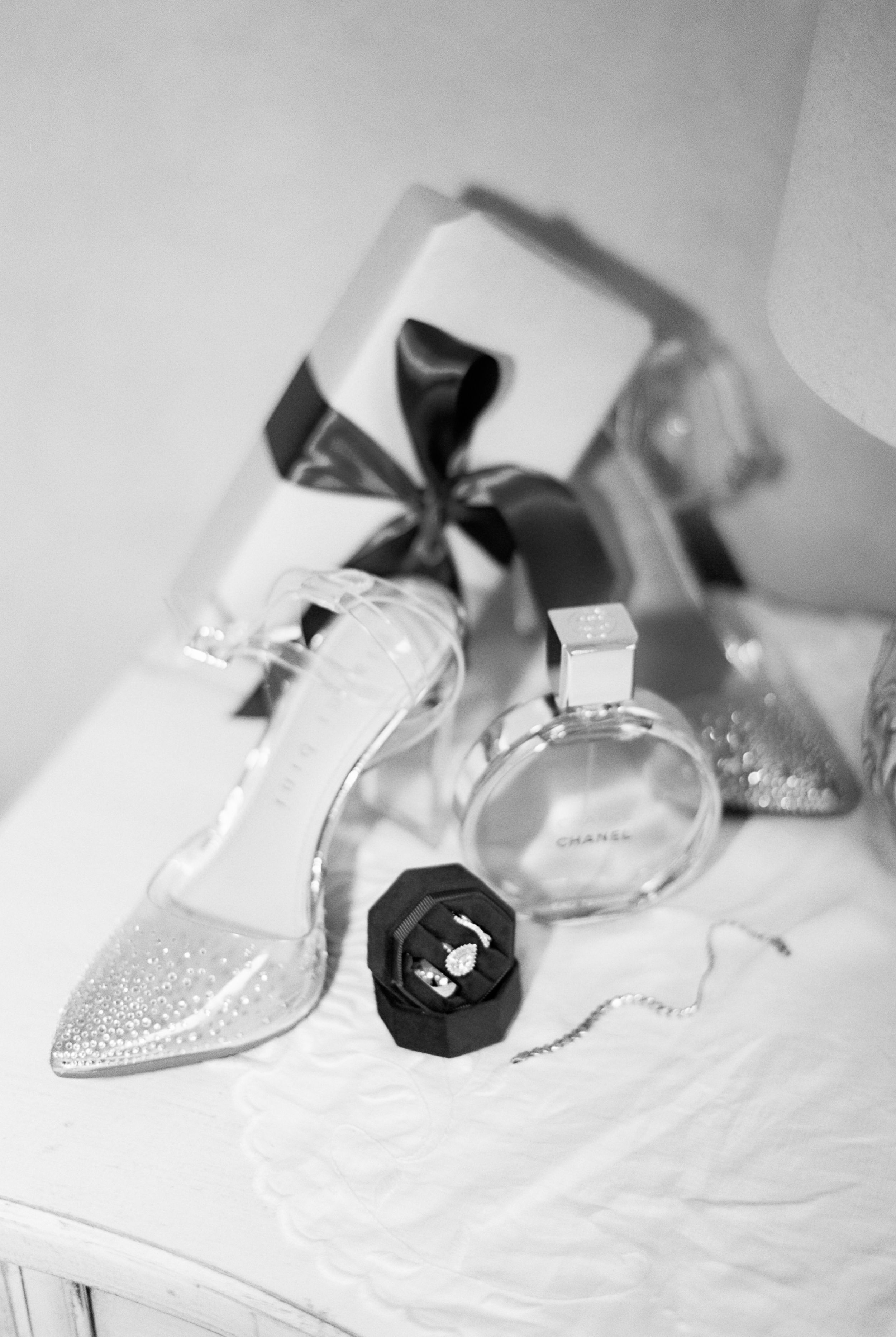 Black and white still life photographs of a perfume bottle and bow arranged artistically on white fabric.