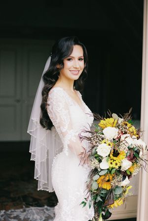 Bride in lace gown holding vibrant sunflower and white rose bouquet.