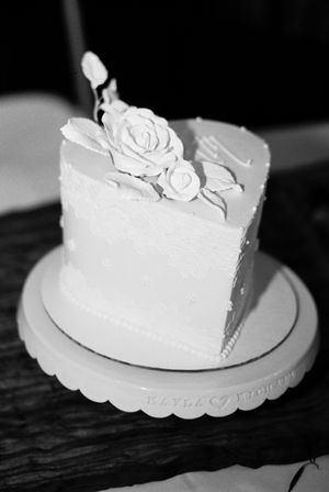 Elegant white wedding cake with rose decorations displayed on a dark wooden surface.