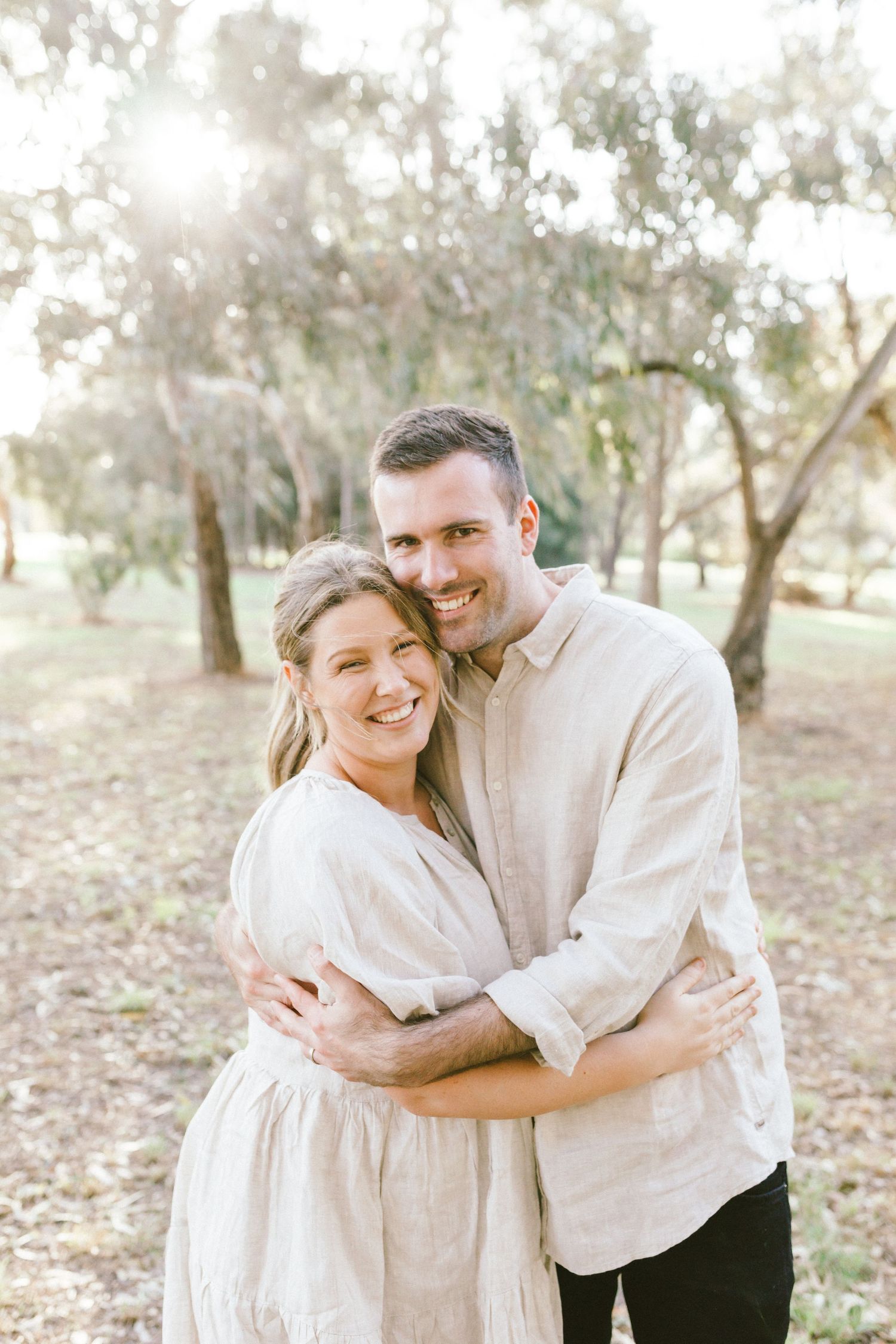 A couple in light colored clothing shares tender embraces while posing outdoors in a natural setting.