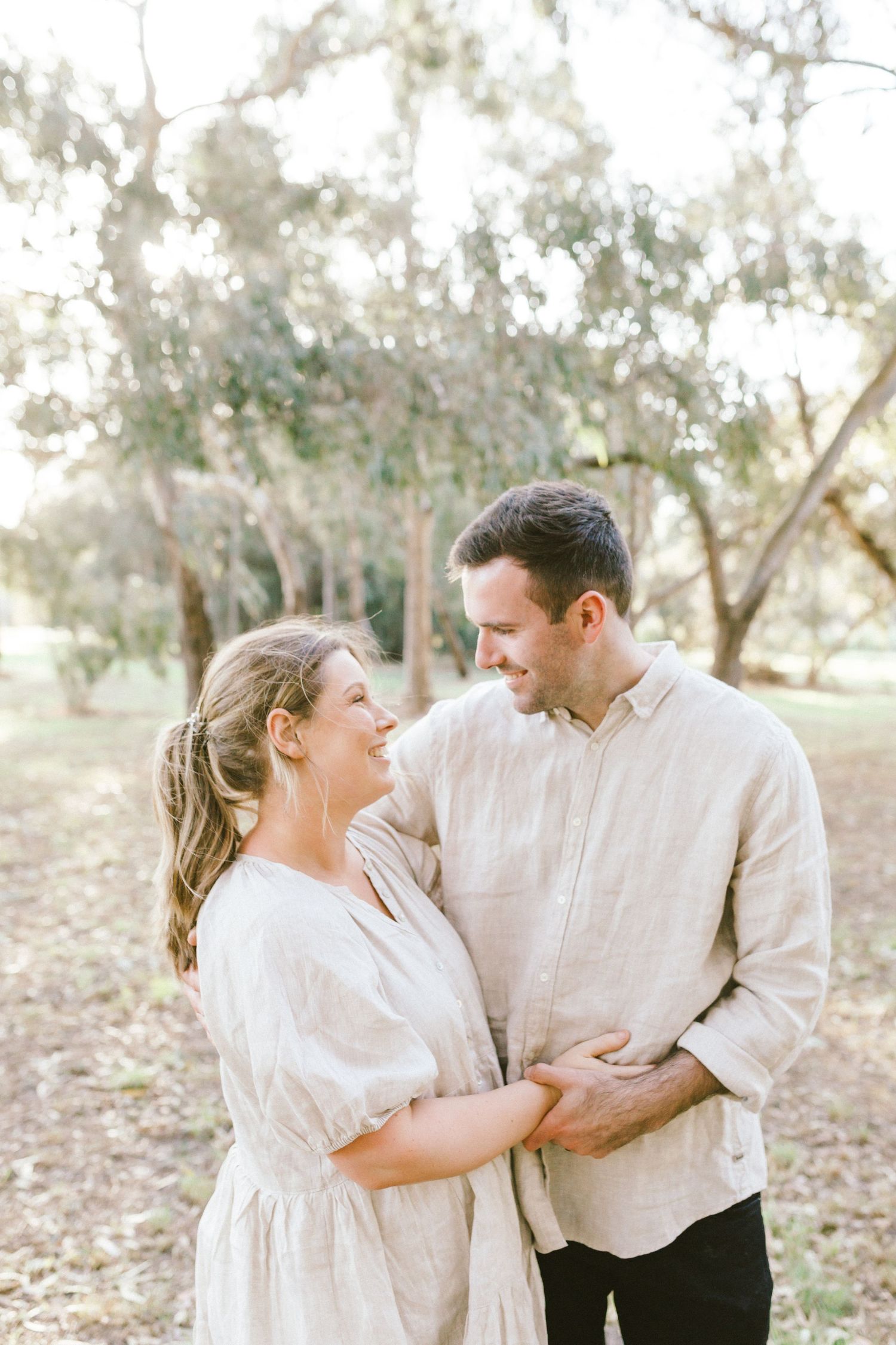 A romantic outdoor couple photoshoot shows a natural, candid interaction between two people in light-colored attire.