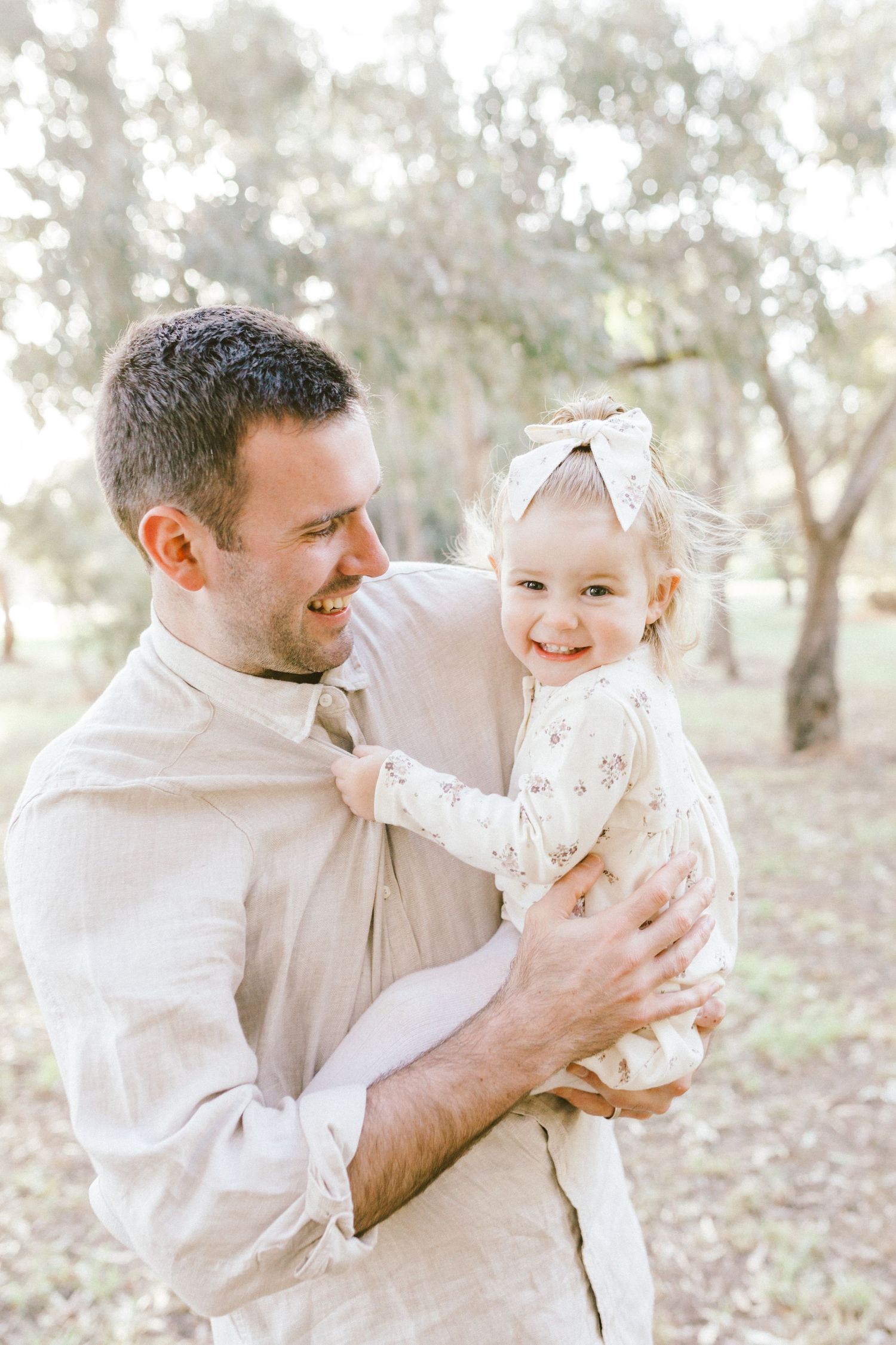 A loving sequence of candid moments between a parent and baby in a sunlit outdoor setting, both wearing light colored outfits.
