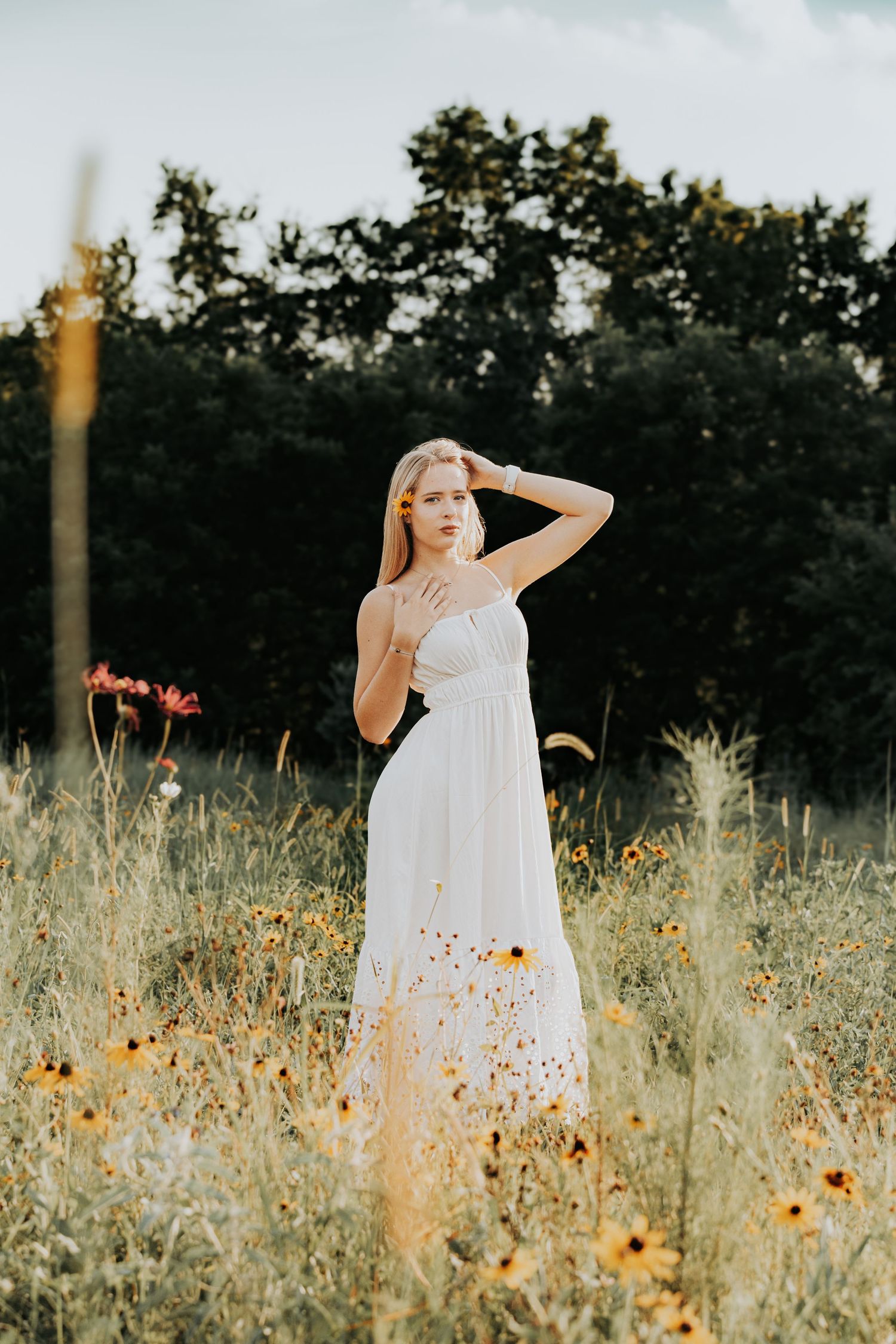 Person in white dress walks through golden wildflower field at sunset with dramatic lighting.